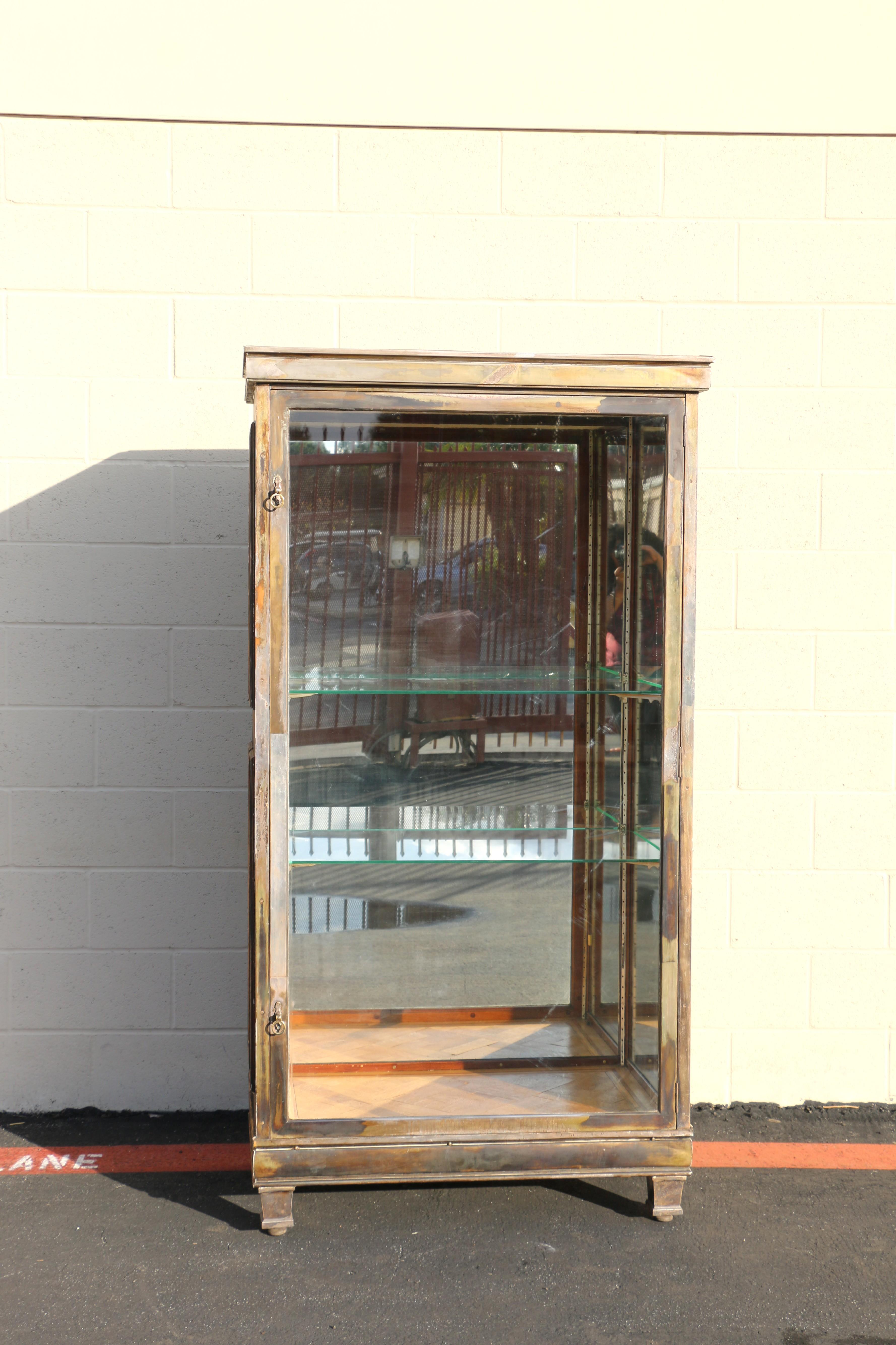 Questa affascinante vetrinetta rustica degli anni '40 è realizzata in mogano massiccio e invecchiata con una finitura naturale. La parte frontale è caratterizzata da finiture in nichel e da un'anta in vetro pieno che si apre per rivelare due ripiani