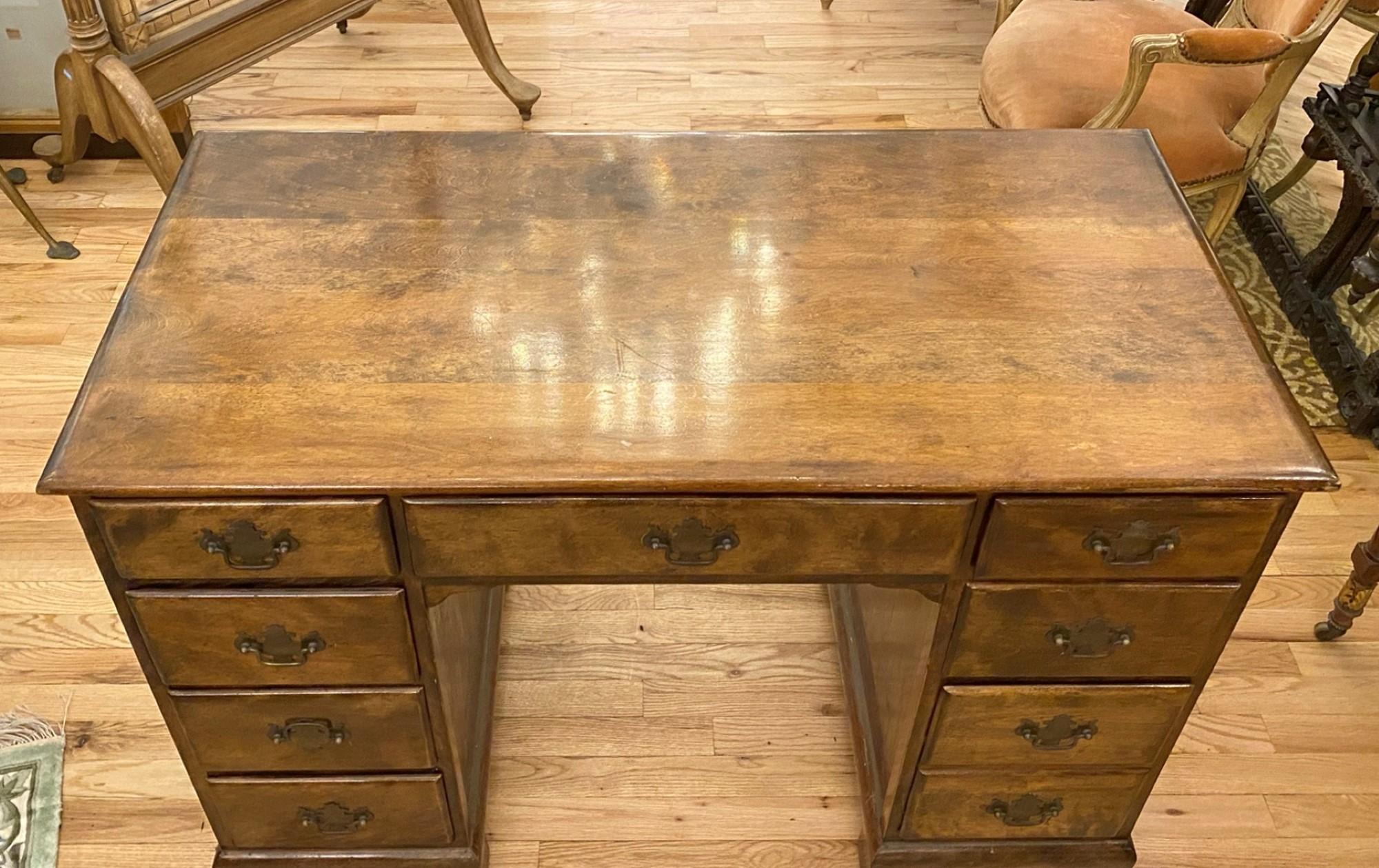 This antique 1940s desk features a center drawer and eight side drawers. Comes with Chippendale style hardware and dovetail joints. Kneehole desks date back to the 18th century and have sets of drawers on either side of the recessed or 