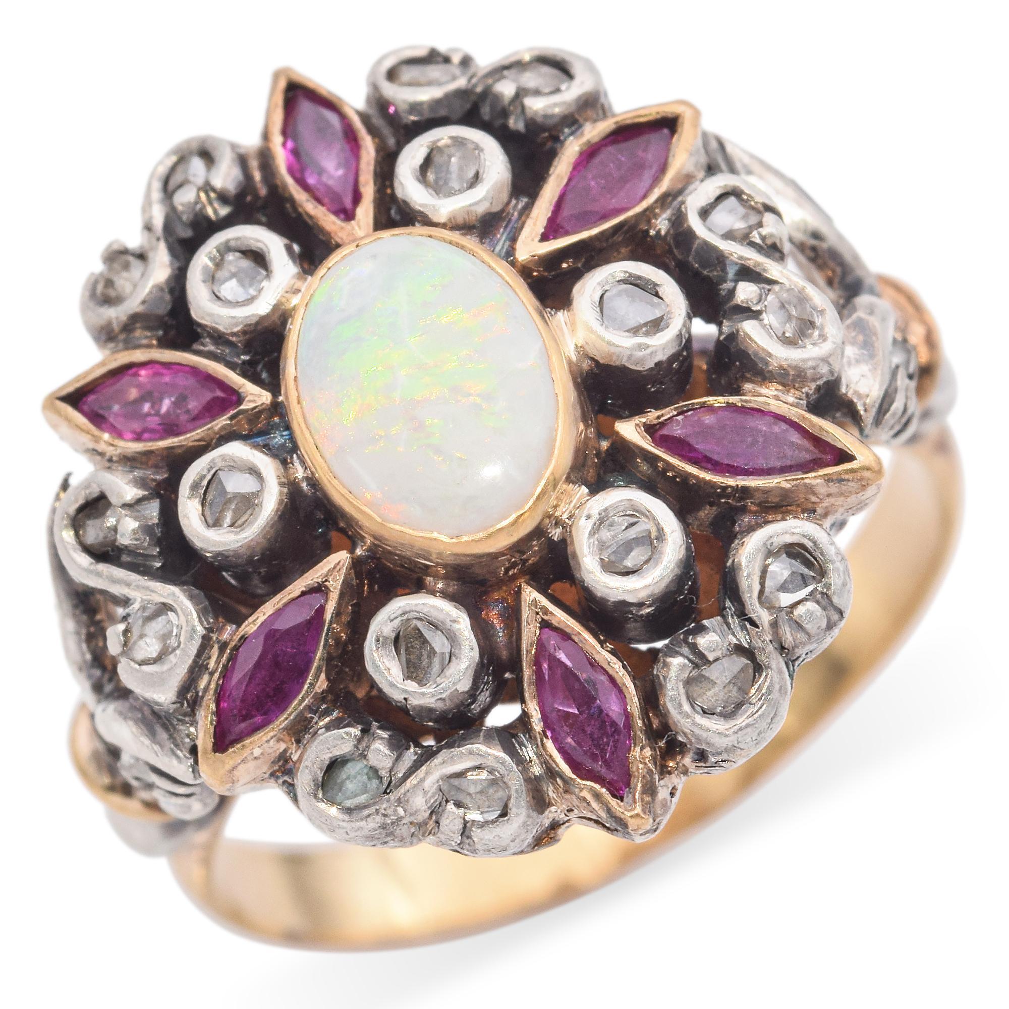 A striking and ornate ring featuring a central oval opal with a captivating play of colors.
The opal is surrounded by marquise-cut rubies, adding a vibrant contrast, and accented by round-cut diamonds in an intricate swirling design.
Crafted with