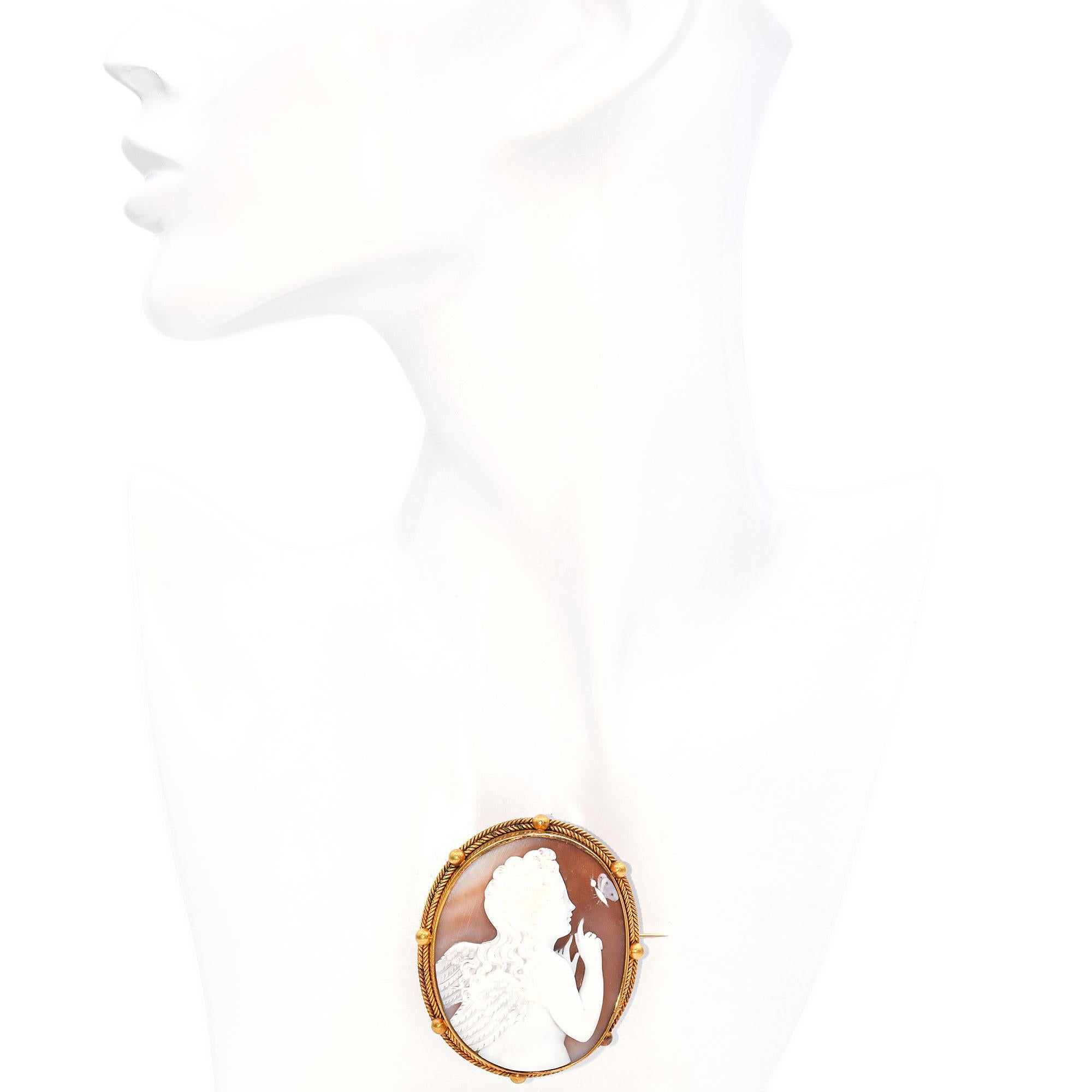 Questa spilla cammeo affascina per la sua intricata lavorazione e il suo design delicato. Realizzato in oro 19 carati, presenta un cammeo finemente intagliato che raffigura una figura angelica con capelli e ali fluenti, in posa serena. La figura