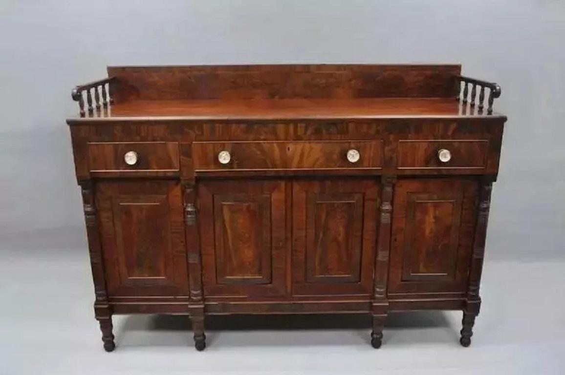 Antique 19th C. American Empire Crotch Flame Mahogany Sideboard Buffet. Item features 2 pull out surfaces on the sides, tall back splash with spindle sides, glass knob pulls, turn carved legs and columns, and large substantial size. Sideboard