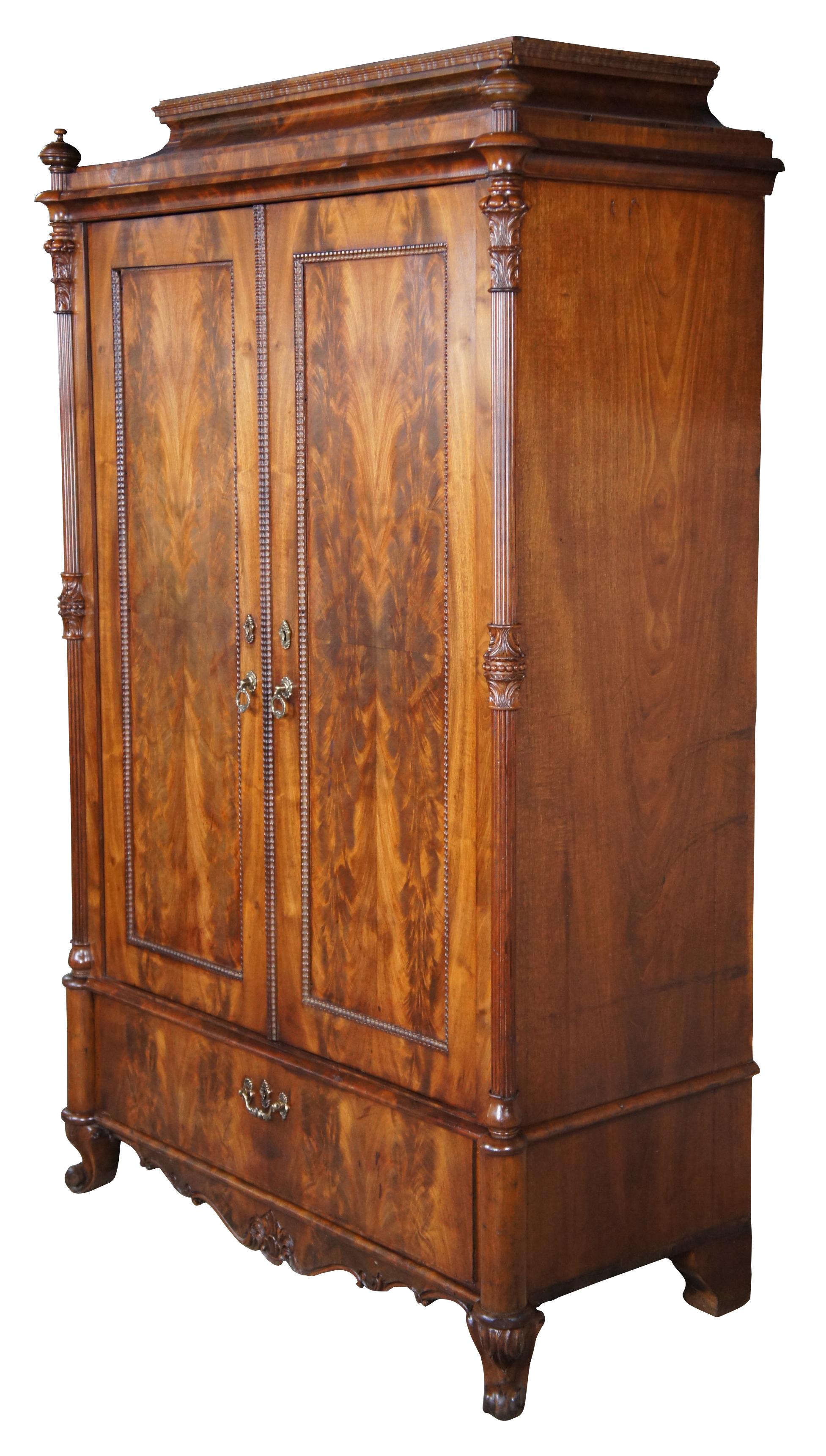 An exquisite American Empire diminutive wardrobe, circa mid 19th century. Made from flame mahogany with double doors over large lower drawer. Features 3/4 cut reeded columns with foliate details, nubby spire finials, ripple trim, brass hardware,
