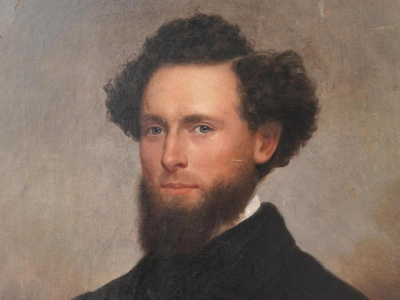 An antique oil painting on canvas laid on board depicting a portrait of a gentleman, circa 1860s. The gentleman is depicted with a beard and curly hair, wearing a black jacket and a black tie. The background is light grayish-brown in an oval.