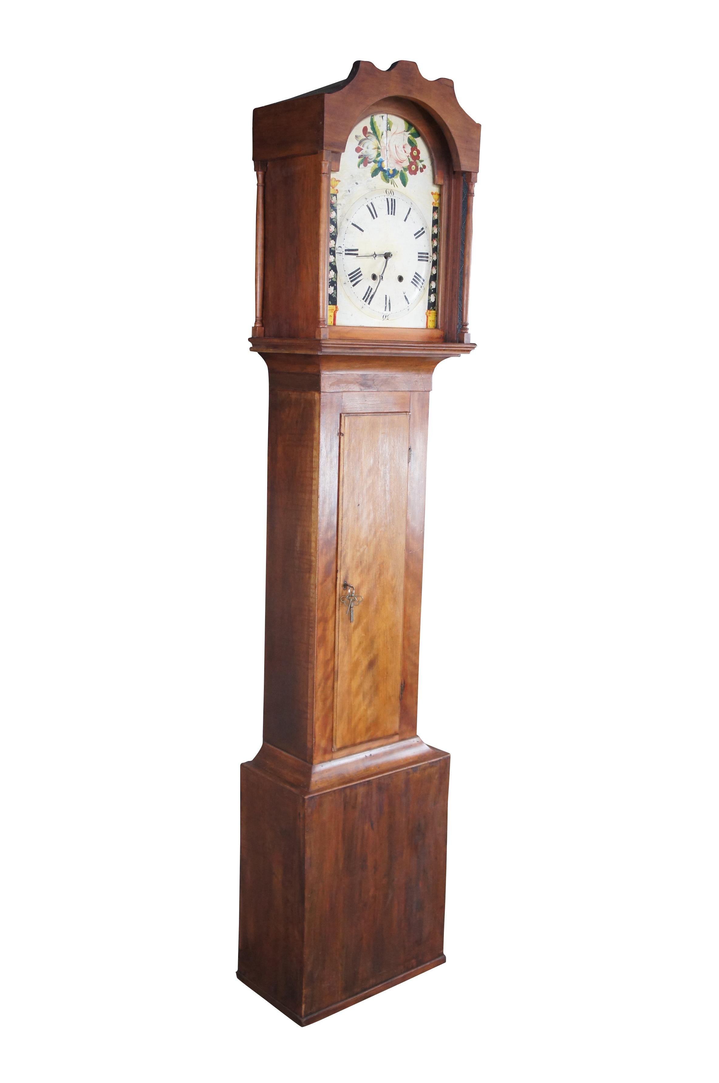 A beautiful tall case clock, circa first half 19th century. Features an American Cherry case with a strip of crotch mahogany veneer below the face. The hand painted face is accented by empire painted columns and a bouquet of flowers at the top.