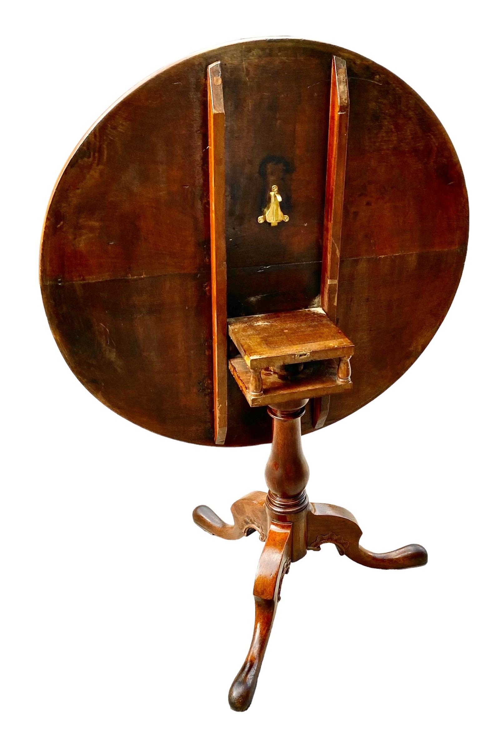 A lovely antique English Georgian hand carved, faded mahogany tilt top, revolving table with a carved tripodal base with pad feet. The top is the most exquisite old, two-board solid faded mahogany making a beautiful presentation. These were used as