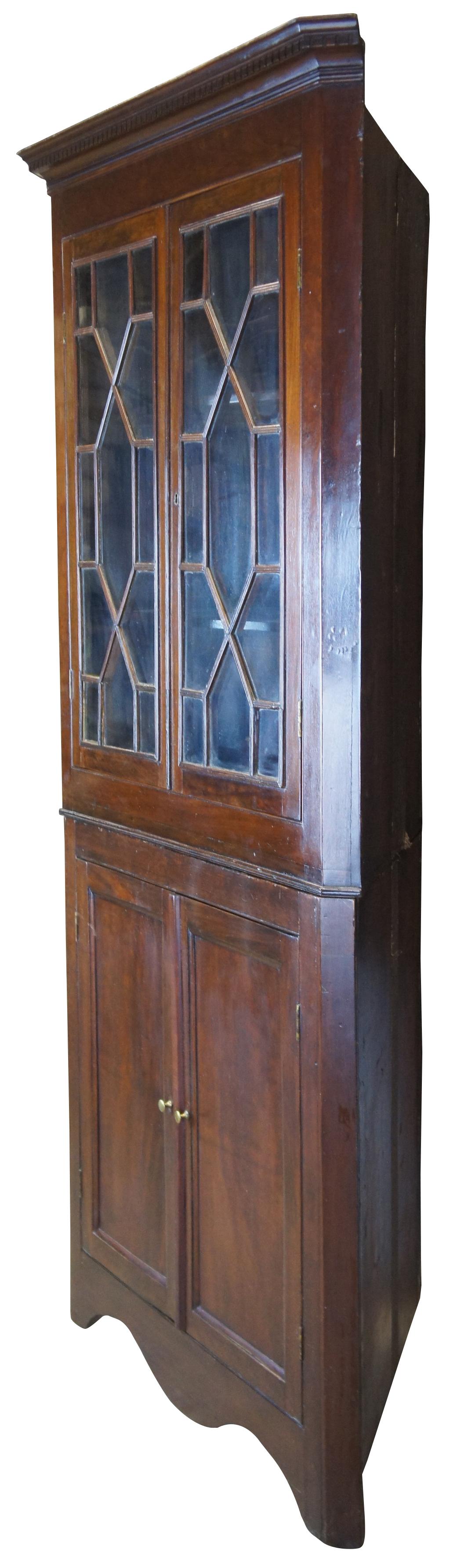 Antique English George III corner cabinet or cupboard. Made of mahogany featuring upper dentil moulding, glazed doors with geometric astragals, that opens to three shelves atop lower cabinet with serpentine skirted base.

Measures: 40