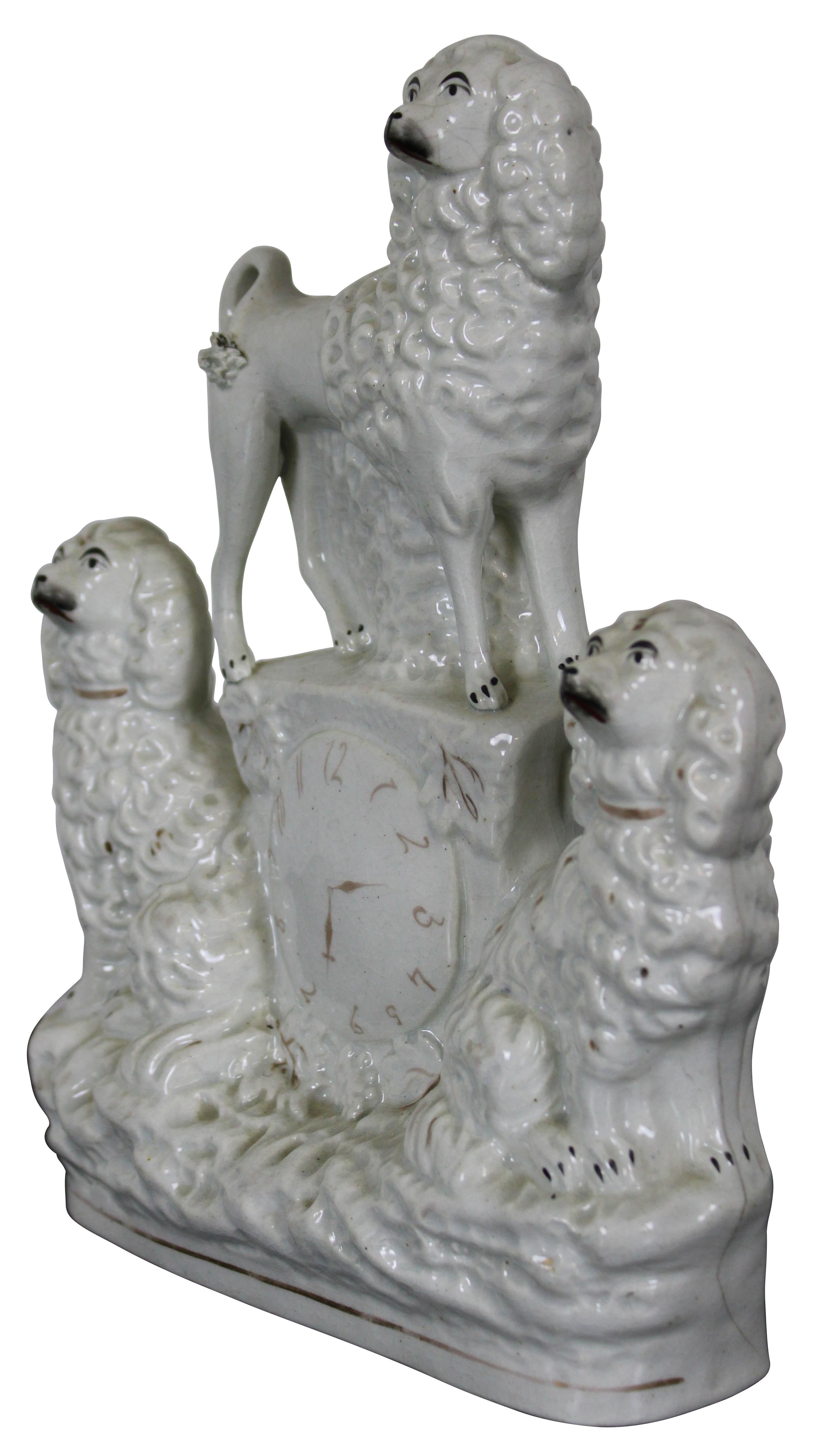 Antique 19th century Staffordshire porcelain figurine featuring a faux clock flanked by a pair of seated King Charles Spaniels and topped with a standing poodle.
 