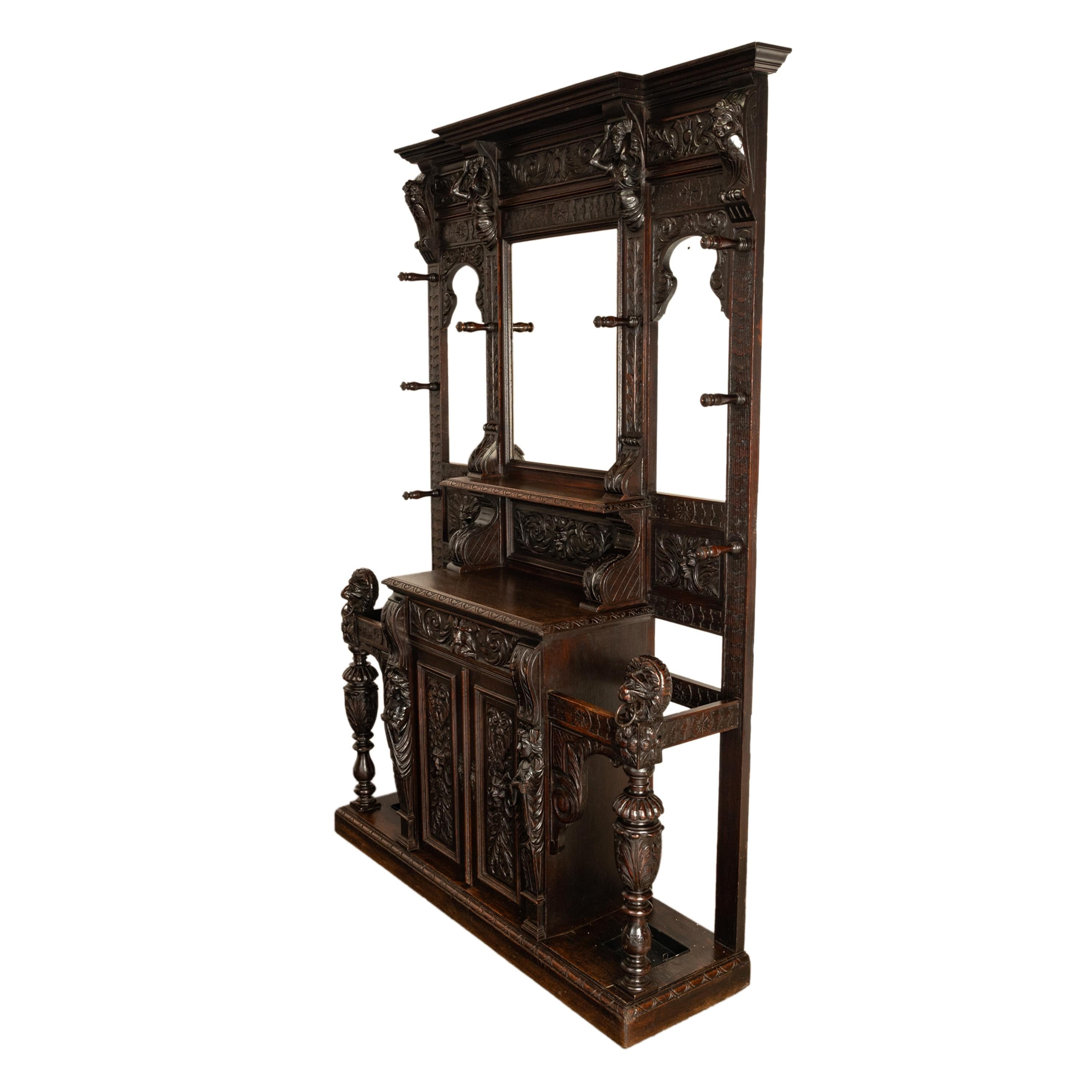 Antique, large & historic, impressively carved oak hall tree, cupboard, umbrella/stick stand, circa 1885.
The hall tree of impressive and significantly carved, to the top is a stepped crown supported by a pair of female figures with their arms
