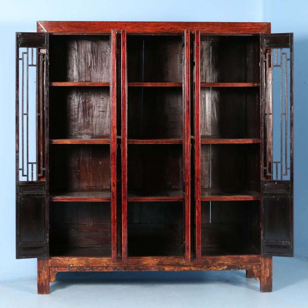 The elongated open panels are visually striking in this stunning cabinet from China. The original red and wood-toned painted finish is slightly distressed, revealing the age and adding depth and character to the cabinet while the lacquered finish