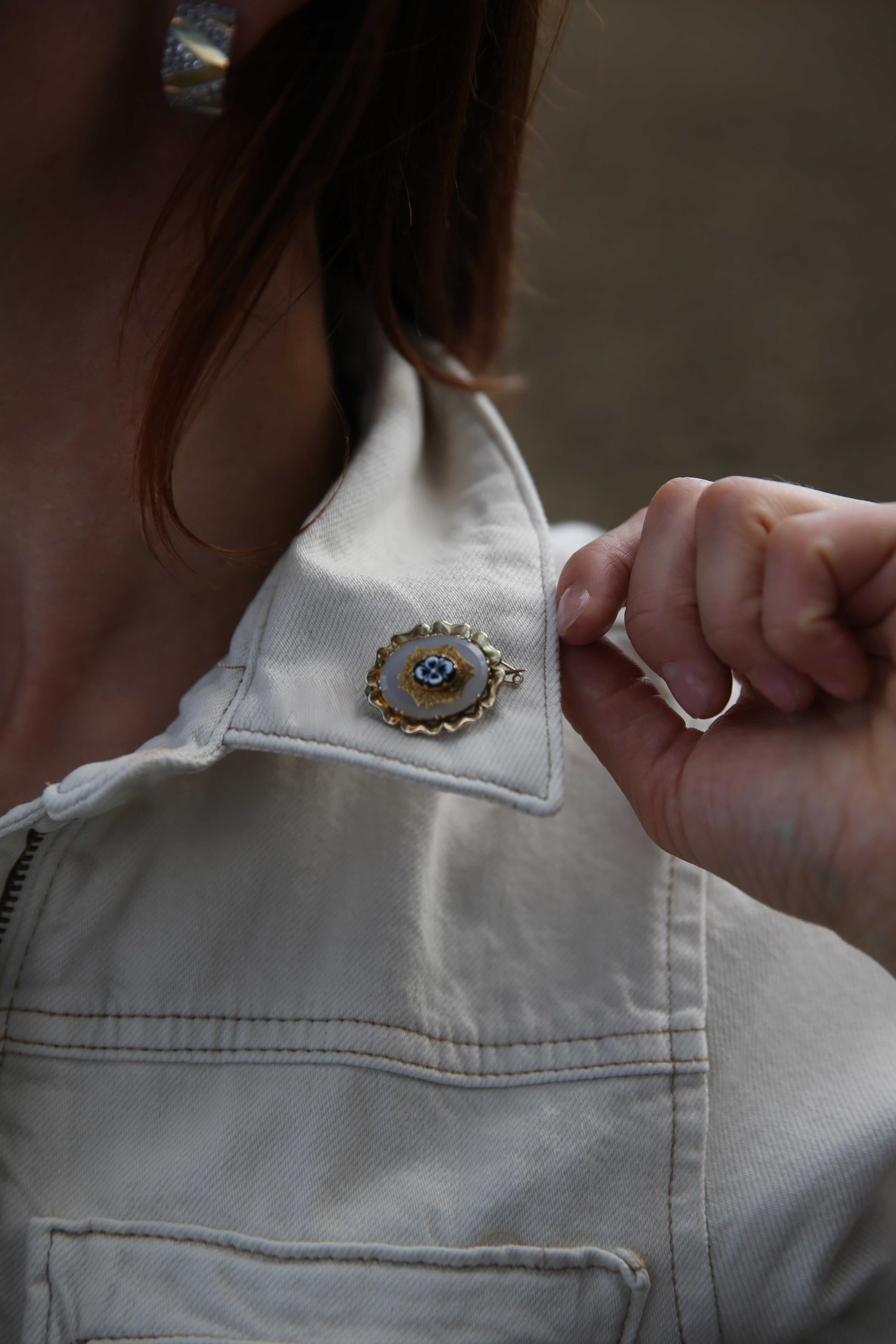 Cette broche de deuil du XIXe si�ècle est réalisée en or jaune 9kt et comporte une plaque ovale en calcédoine montée avec un motif floral en agate sculptée. La broche est encadrée d'une bordure dorée légèrement festonnée avec des détails gravés,