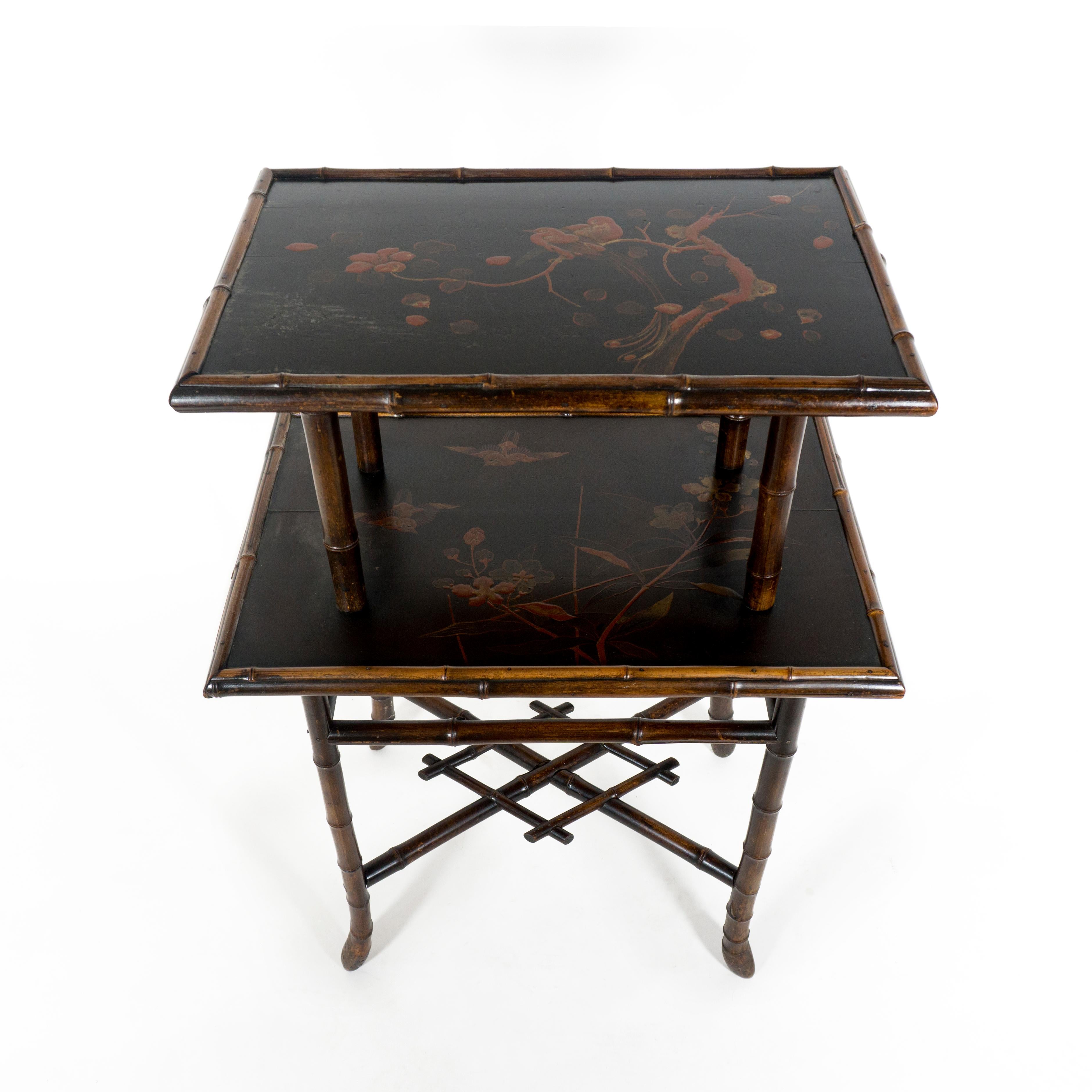 Charming and highly decorative chinoiserie bamboo side table with two lacquered tiers. 
Both shelfs are hand painted in blacks and reds and gold and for its age the the colors of the bird and flowers are still vibrant. The final varnish shows signs