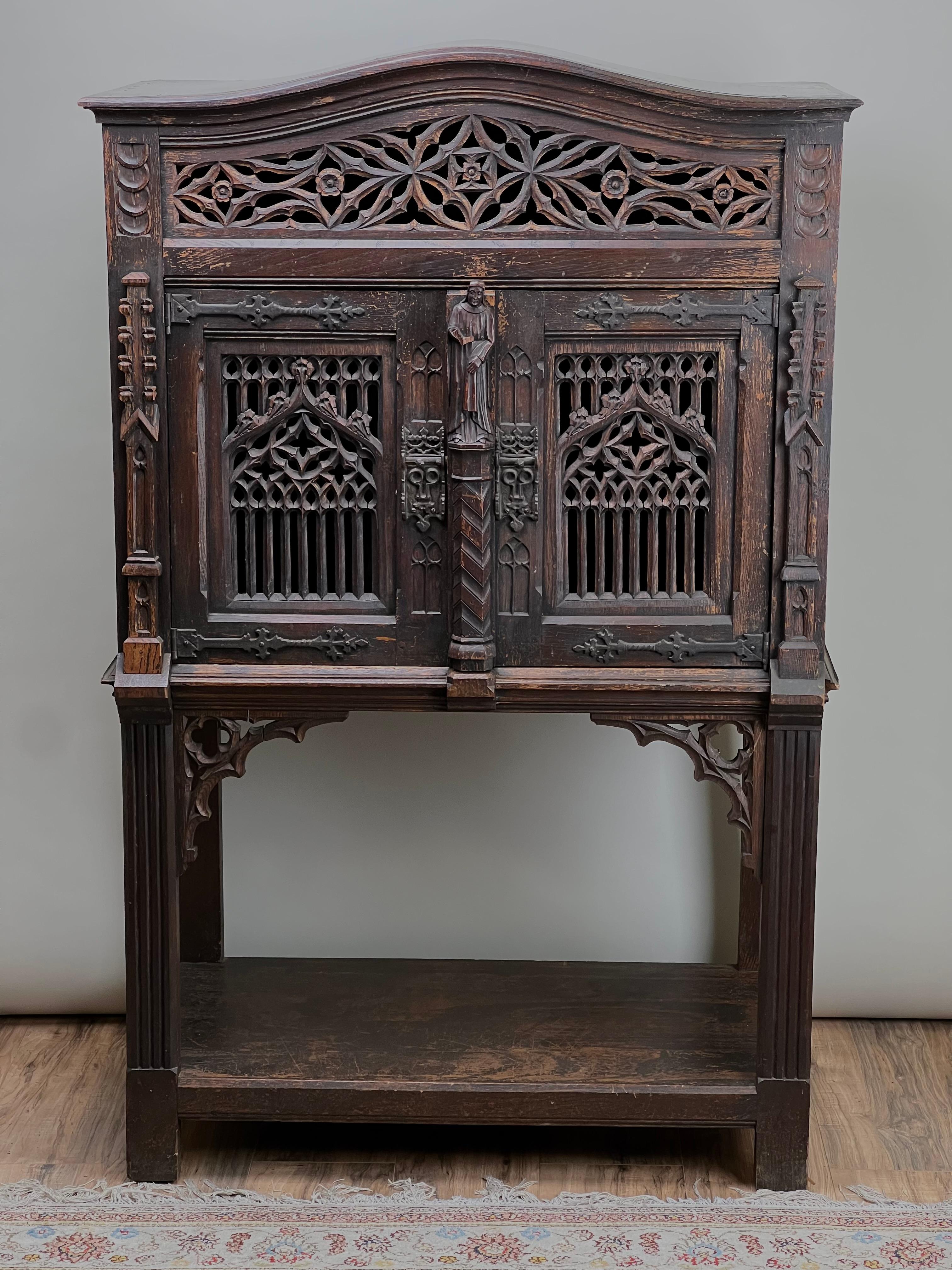 Cette armoire de cour de style néo-gothique belge du XIXe siècle est un témoignage exquis de l'artisanat élaboré de l'époque. Sculptée dans un bois riche et sombre, elle présente les éléments quintessentiels du style néo-gothique, tels que les arcs