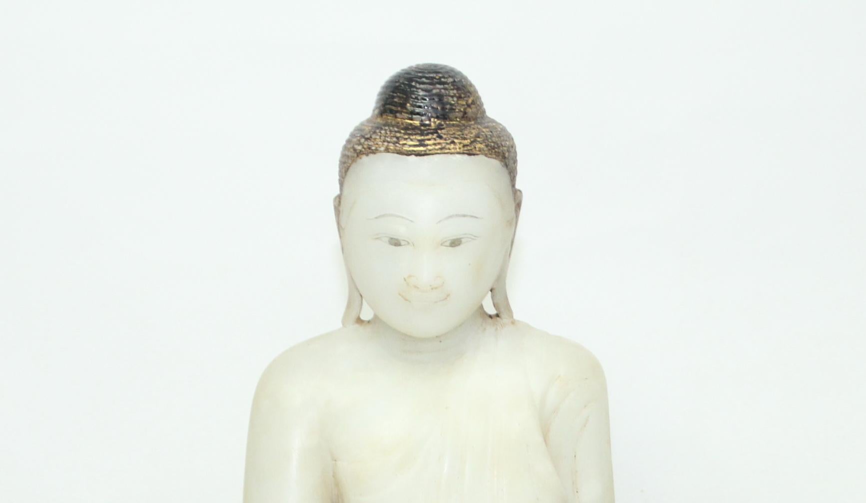 The Buddha is seated on a low, lotus base in vajrasana (lotus) position with bhumisparsha mudra, in which the finger-tips of the right hand touch the earth to symbolize the moment of enlightenment. The Buddha has a serene expression and is clothed