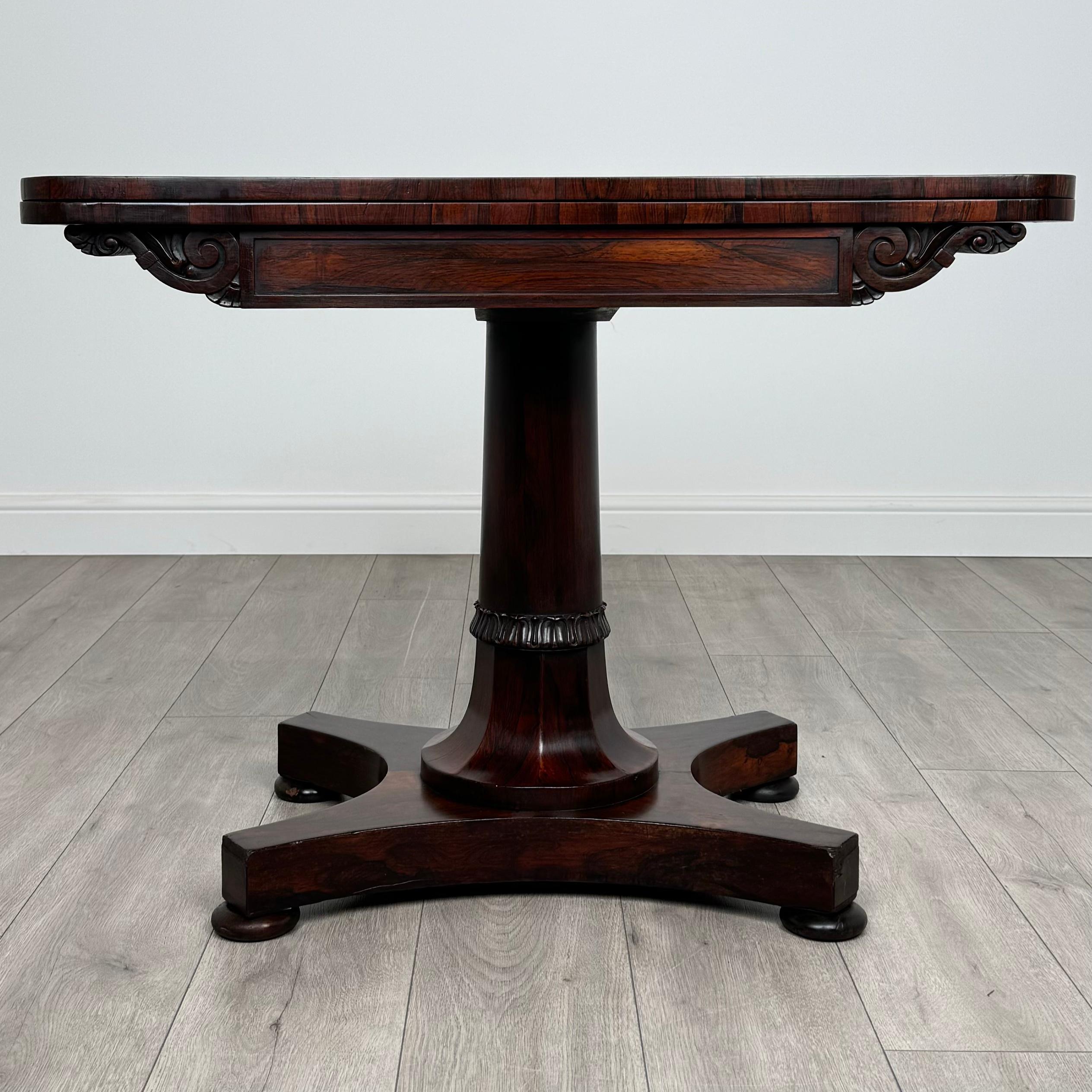 Cette table à cartes ancienne du XIXe siècle, fabriquée en bois de rose, est une pièce étonnante d'une qualité et d'un design exceptionnels. 
Posée sur une solide base en pilier avec d'élégants pieds en chignon, la table présente de subtiles