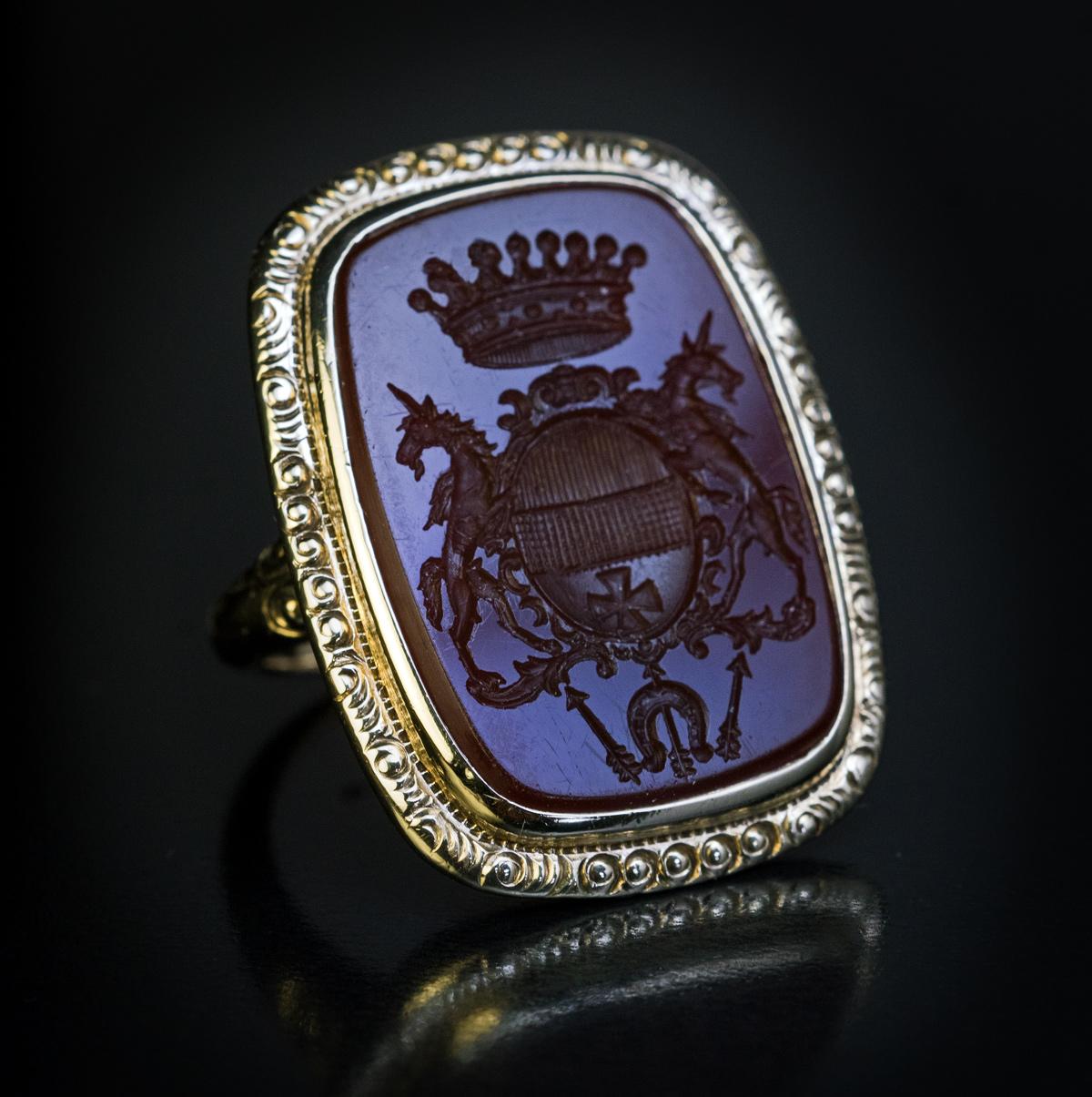 Circa 1880

A Victorian era antique 14K gold signet ring is set with a large chocolate brown carnelian seal matrix finely engraved with a coat of arms of a Count or a Baron. The armorial is designed as a crowned shield with a cross held by two