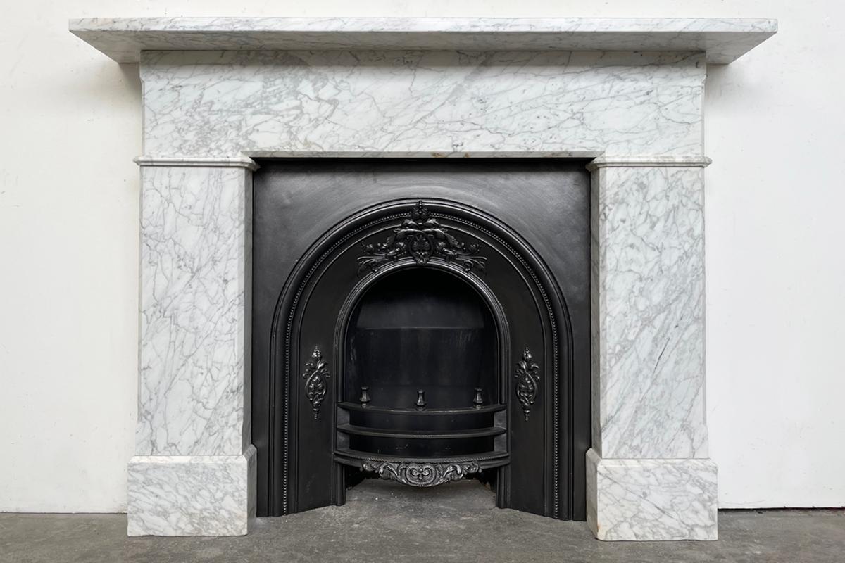 AAntique 19th-century Carrara marble fireplace surround of simple form and good proportions. With a full frieze above plain jambs and boxed plinths. Circa 1860.

Pictured with an original Victorian arched cast iron grate, sold separately.

For