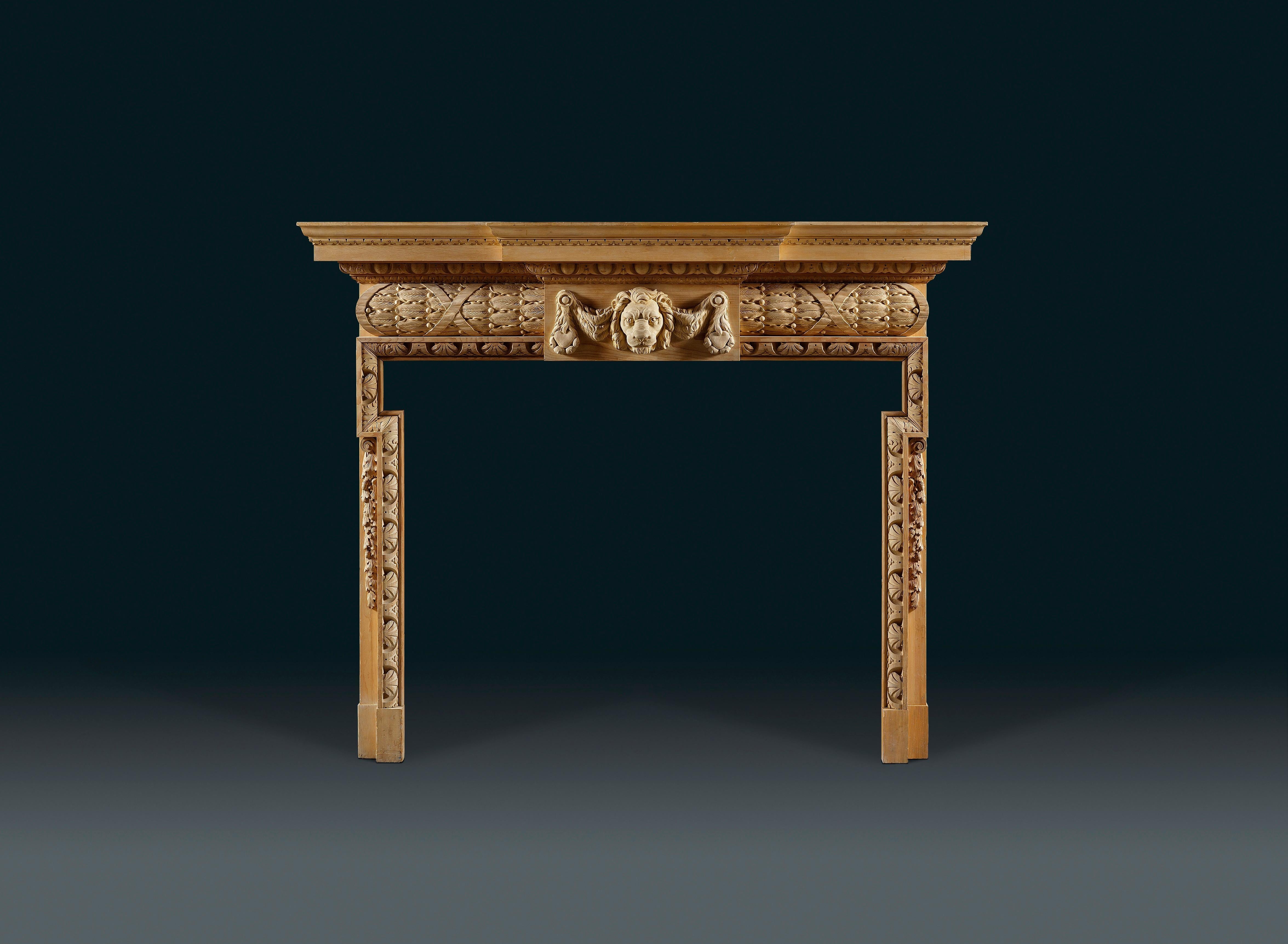 The simple break-front shelf sits above bold egg and dart moulding and a central tablet carved with a Nemean lion mask set against a stiff-leaf barrel frieze. The dog leg opening is framed by a border of stylised acanthus leaves, with a garland of