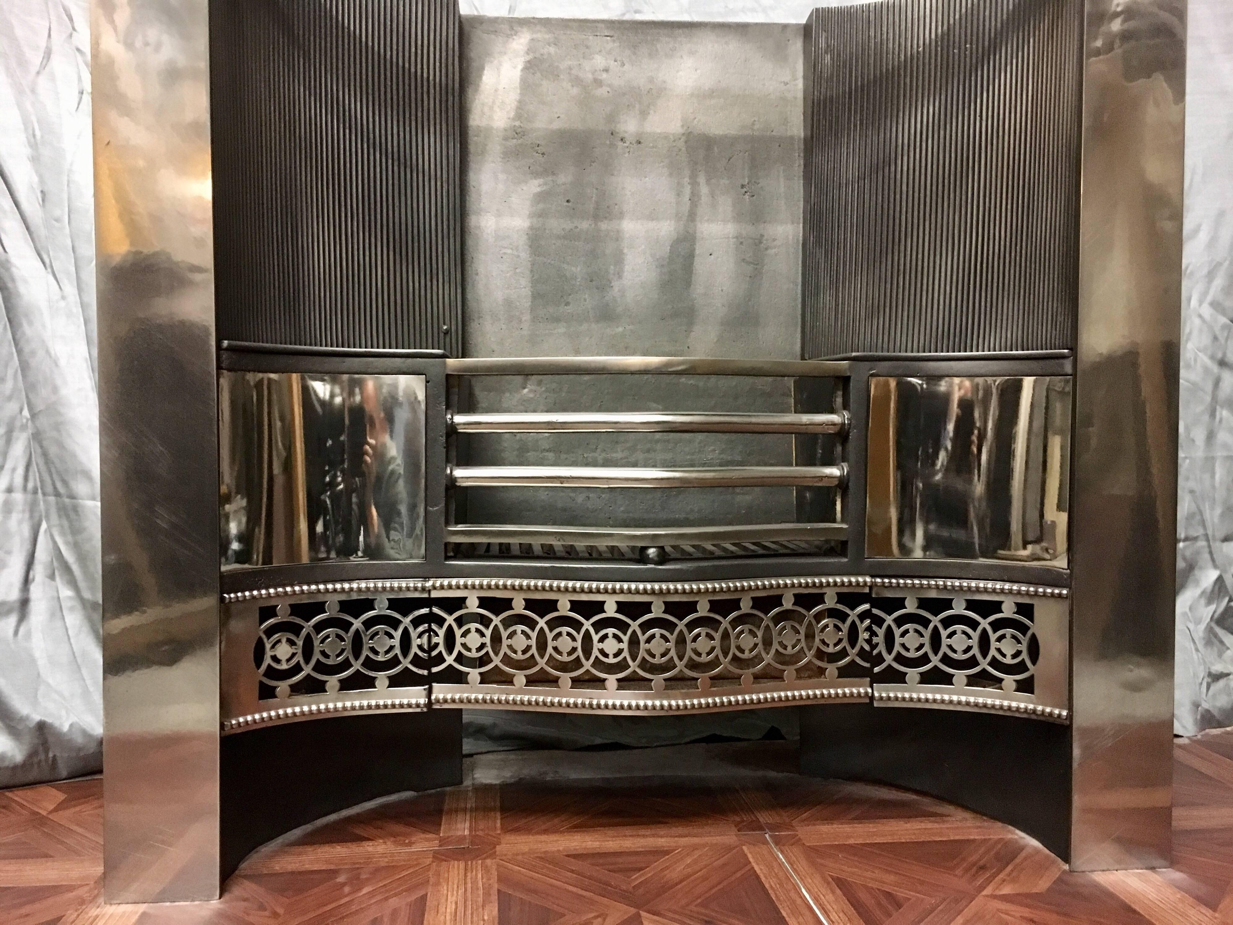 A fully restored and polished antique 19th century cast iron Georgian fire place insert. A polished four barred serpentine grate flanked by convex side panels above a serpentine pierced apron of linked circles framed by repeating gadrooned balls. A