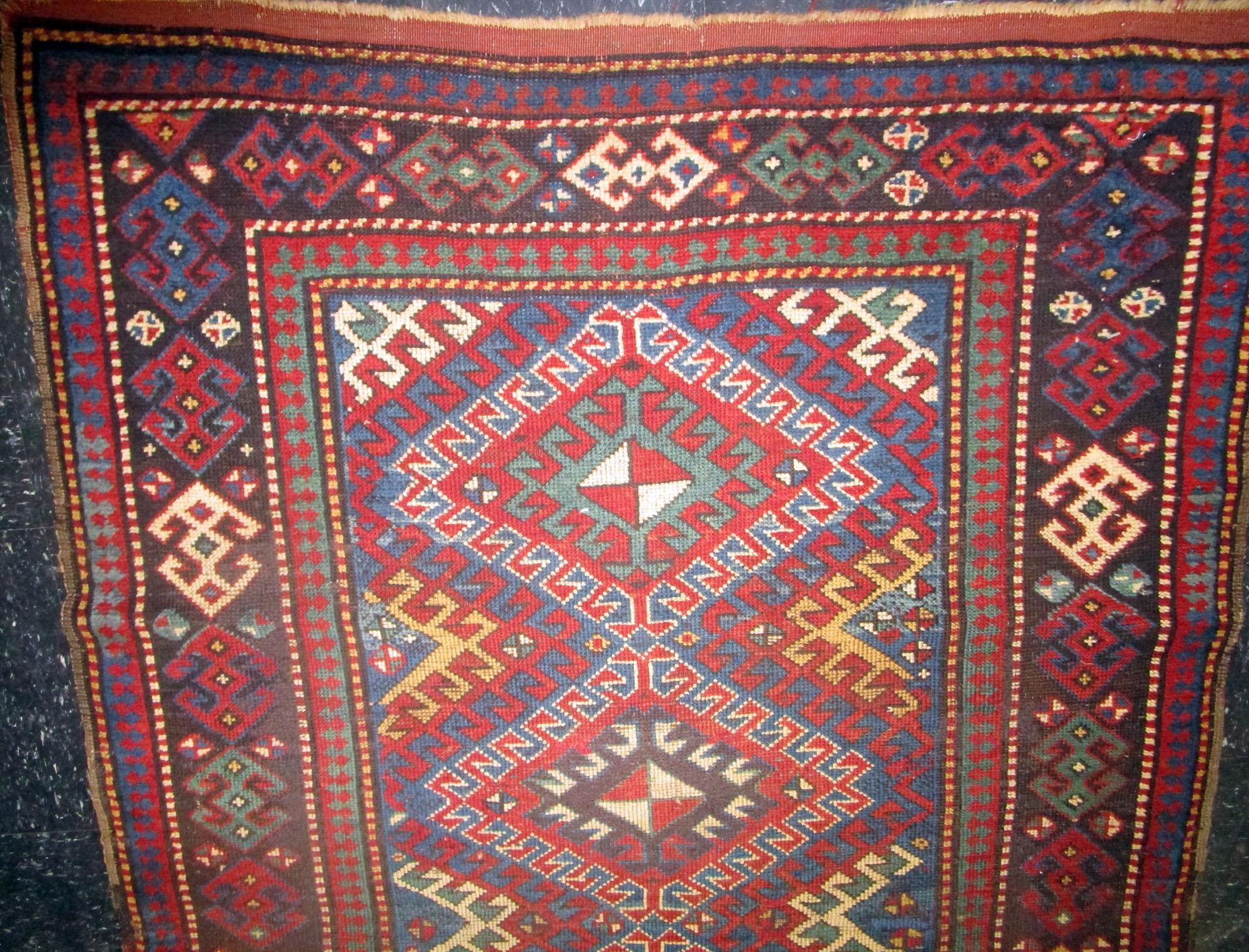 This handsome Kazak rug features a big, bold, dominating geometric diamond pattern with a smaller patterned backdrop, giving it an edge that differentiates it from other rugs on the market. The colors used are vibrant via the rug’s denser dyes, with