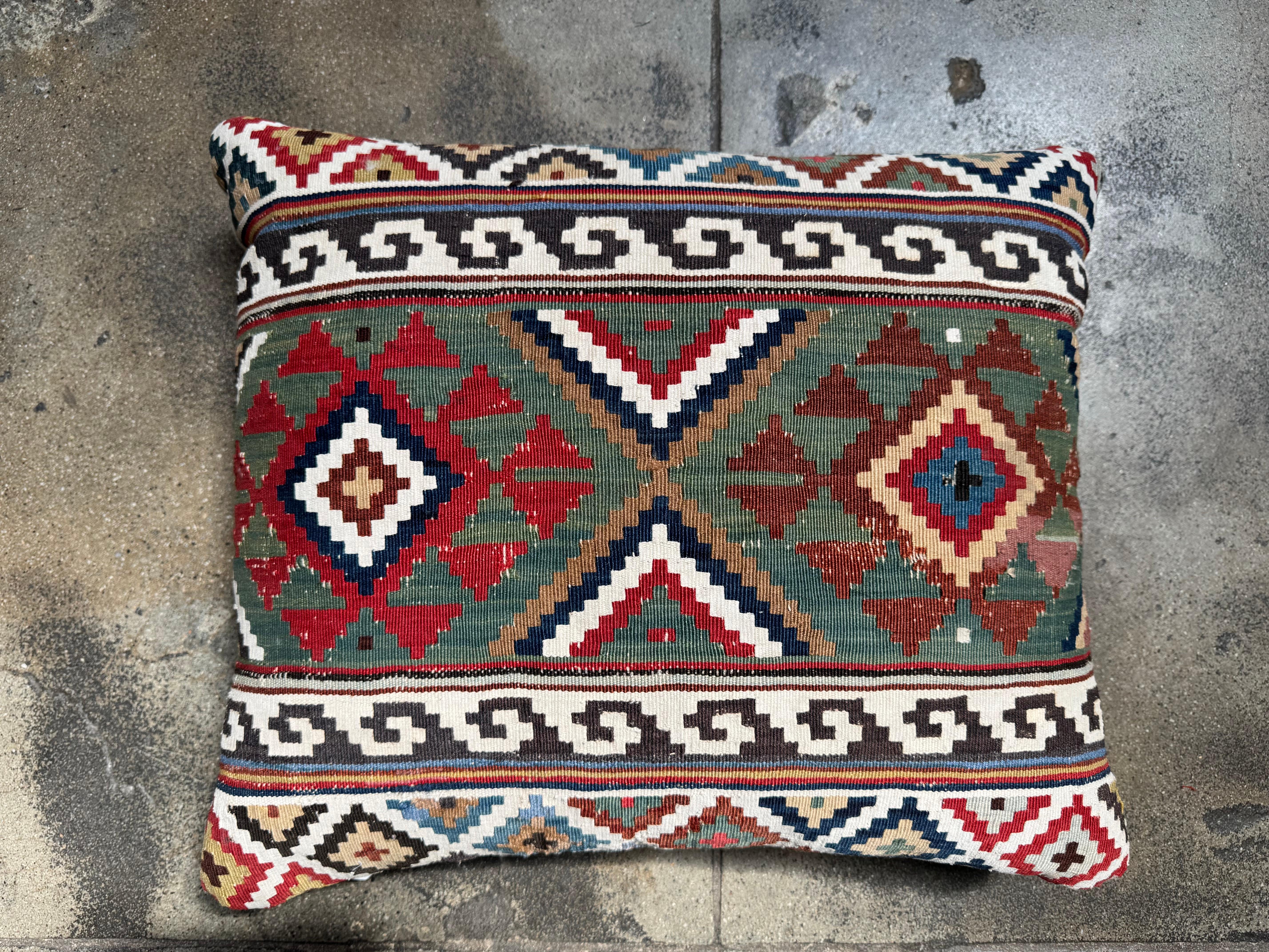 Questo antico cuscino kilim caucasico del XIX secolo è un pezzo tessile vibrante e ricco di dettagli, tessuto a mano con audaci simmetrie geometriche e motivi simbolici. I medaglioni centrali a forma di diamante sono affiancati da motivi tribali