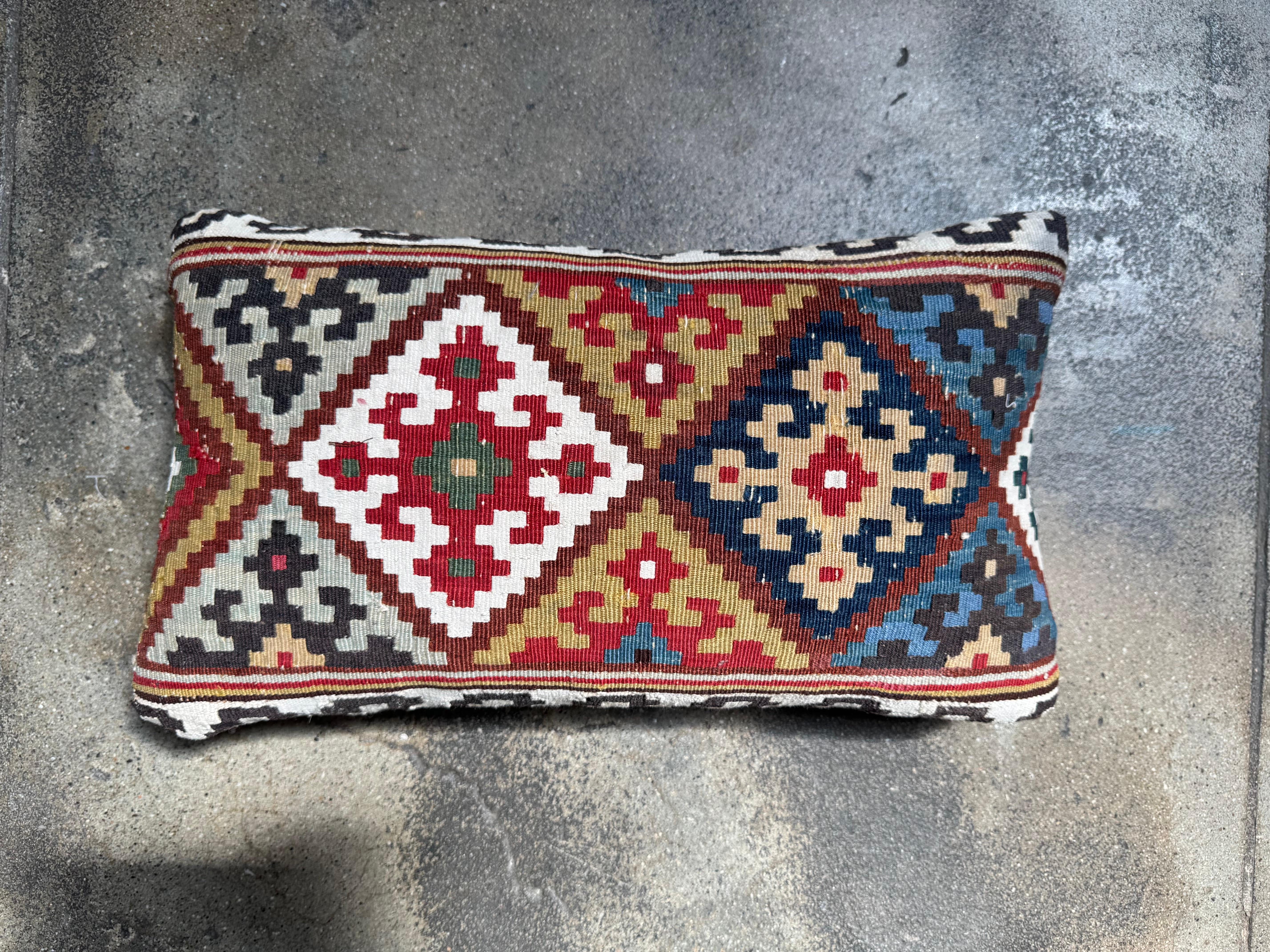 Rich with history and intricate craftsmanship, this 19th century Caucasian kilim pillow is a striking showcase of traditional tribal design. Handwoven from antique wool textiles, it features two large central diamond medallions, framed by linear