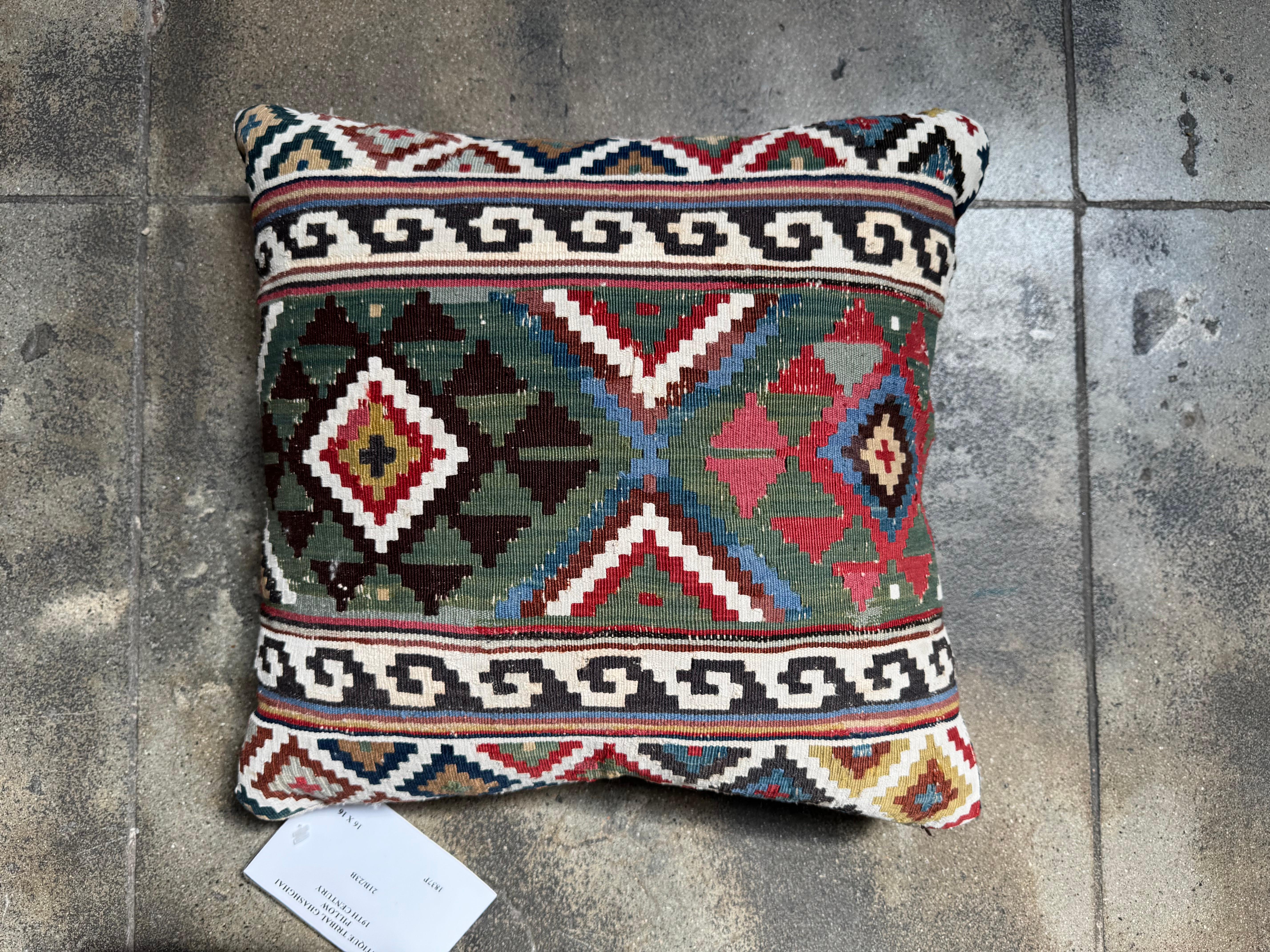This antique 19th century Caucasian kilim pillow is a striking fusion of bold pattern and artisanal history. Handwoven from richly pigmented wool, the pillow features central diamond and triangular motifs framed by traditional scrolling borders. The