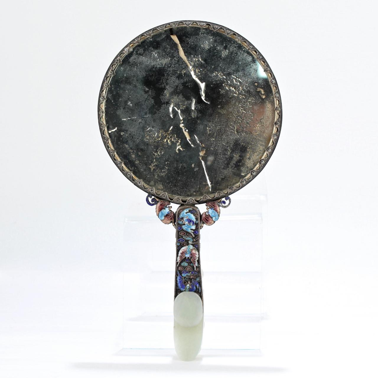 A wonderful, antique Chinese silver and jade hand mirror.

The silver is decorated with enamel, a jade or jadeite medallion at the center, and a ring of cabochon cut semi-precious gemstones (and/or glass beads) .

The handle is mounted with an