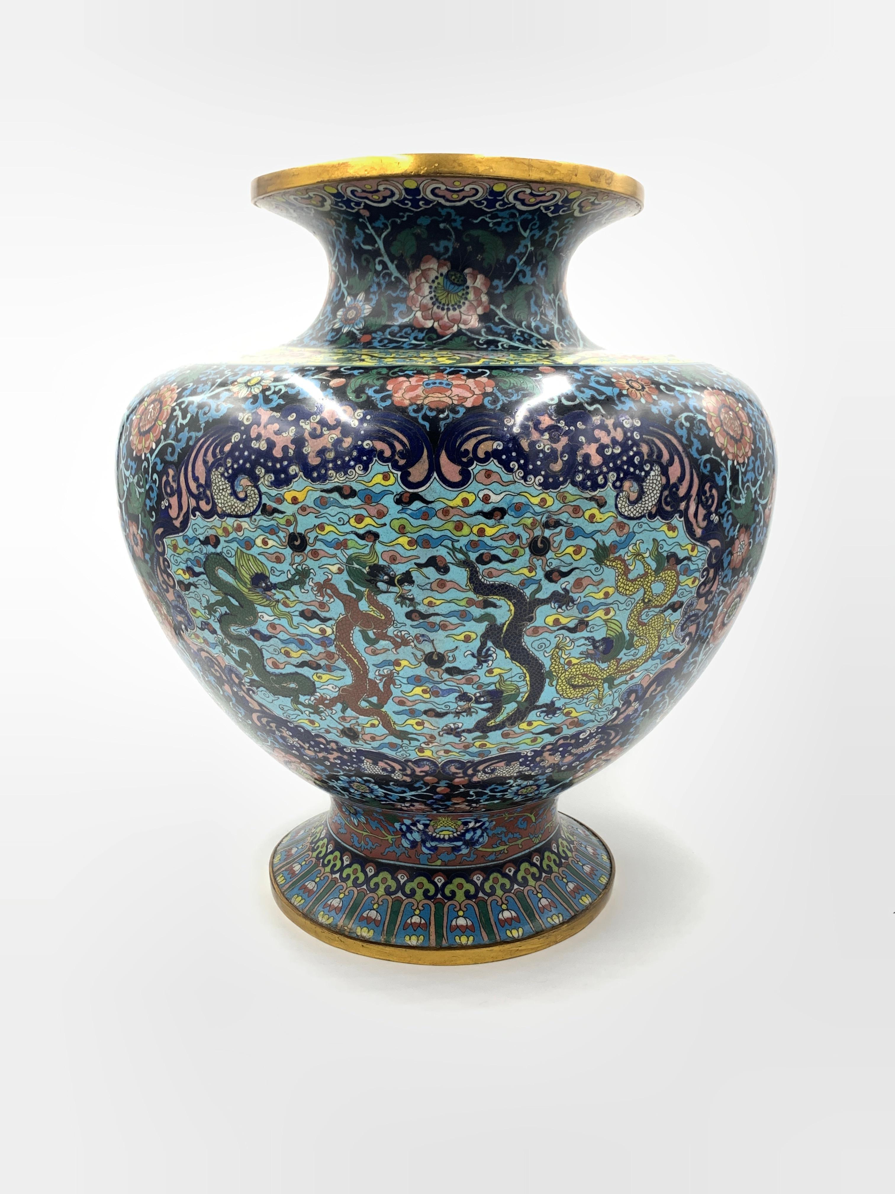 This Chinese vase is made of brass with a lovely enamel cloisonné floral design. The elegant vase sits on a narrow round base with a short funnel neck. The cloisonne floral and leaf patterns are carefully detailed and feature beautiful, vibrant, and