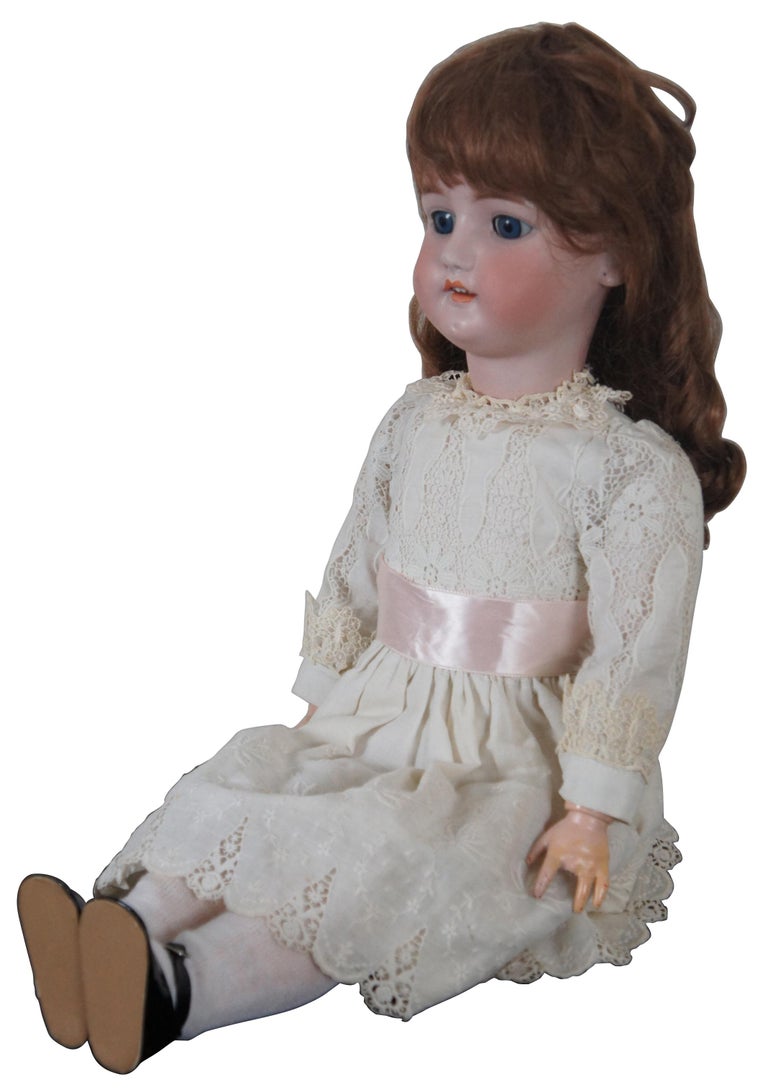 Antique German bisque head doll by CM Bergmann with composite body and articulated jointed limbs, sleep eyes, marked “CM Bergmann Simon & Halbig 12” on the back of the neck and dressed in white lace dress with pink sash. “Charles M. Bergmann