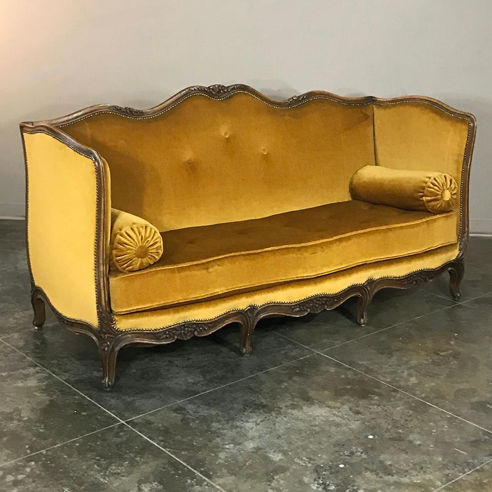 Upholstered in sumptuous mohair, this antique 19th century country French sofa features a delightful Louis XV-inspired styling! The undulating naturalistic form of the framework exudes delight and completely envelopes the entire piece with four