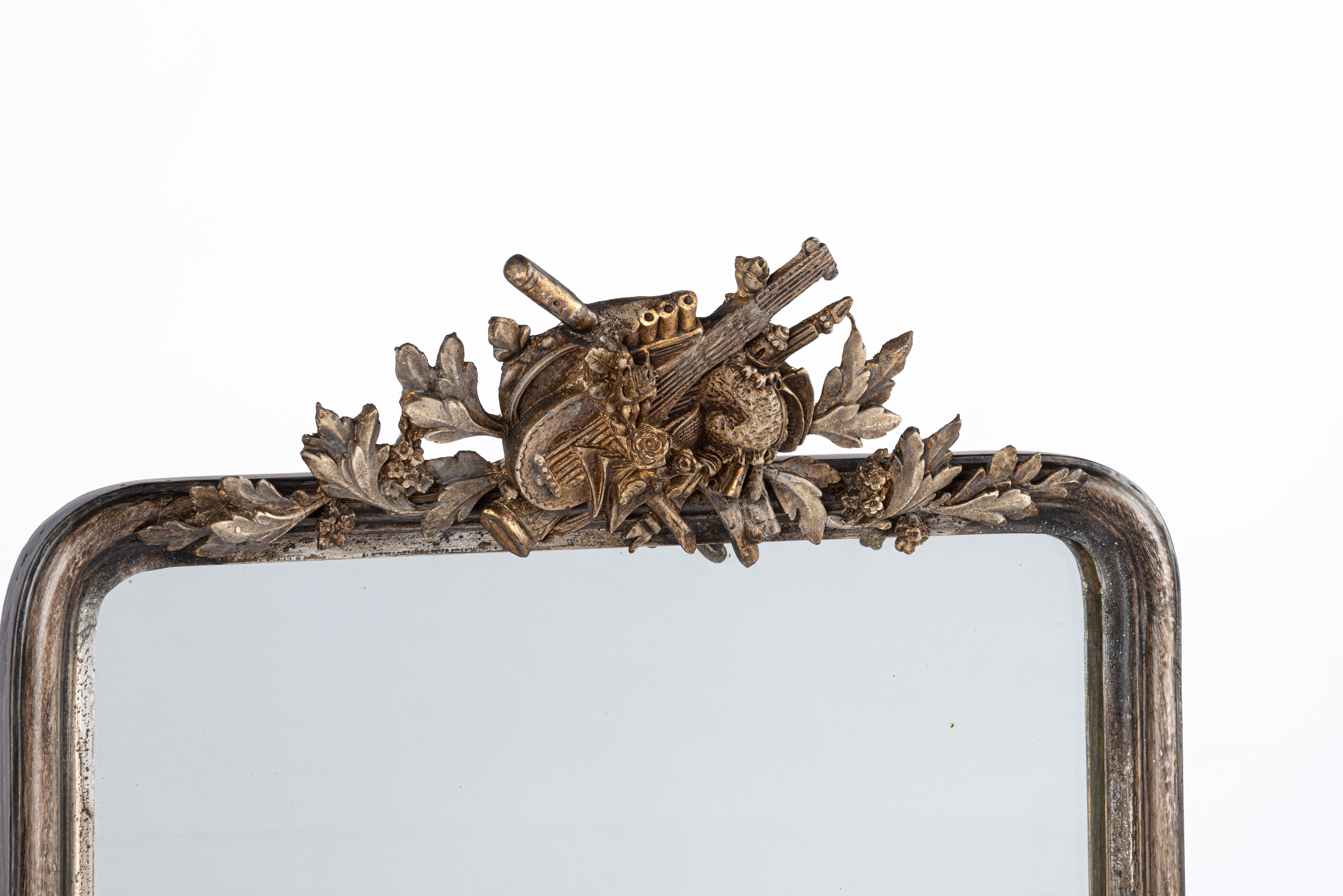 On offer here is a very handsome and tall pier mirror that was made in the late 19th century in Northern France. Its sleek frame with upper rounded corners is typical for the Louis Philippe style. The elaborate crest features a rich variety of