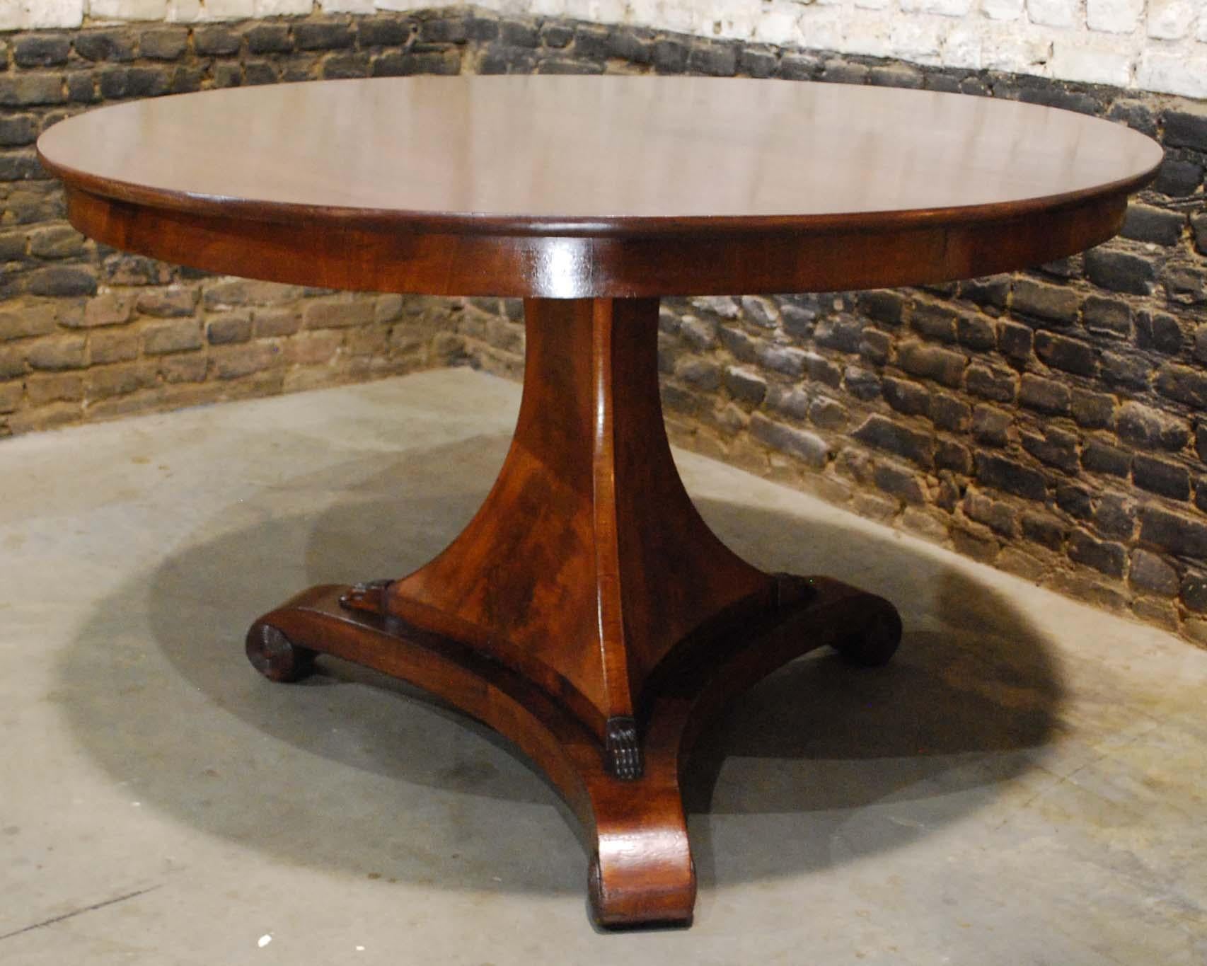 A beautiful round mahogany dining table on a trefoil platform base that ends in elegant scrolls.
The base has an elegant triangular column that ends in claw feet to support the tabletop. The tabletop is made in 0.8-inch thick solid mahogany in a