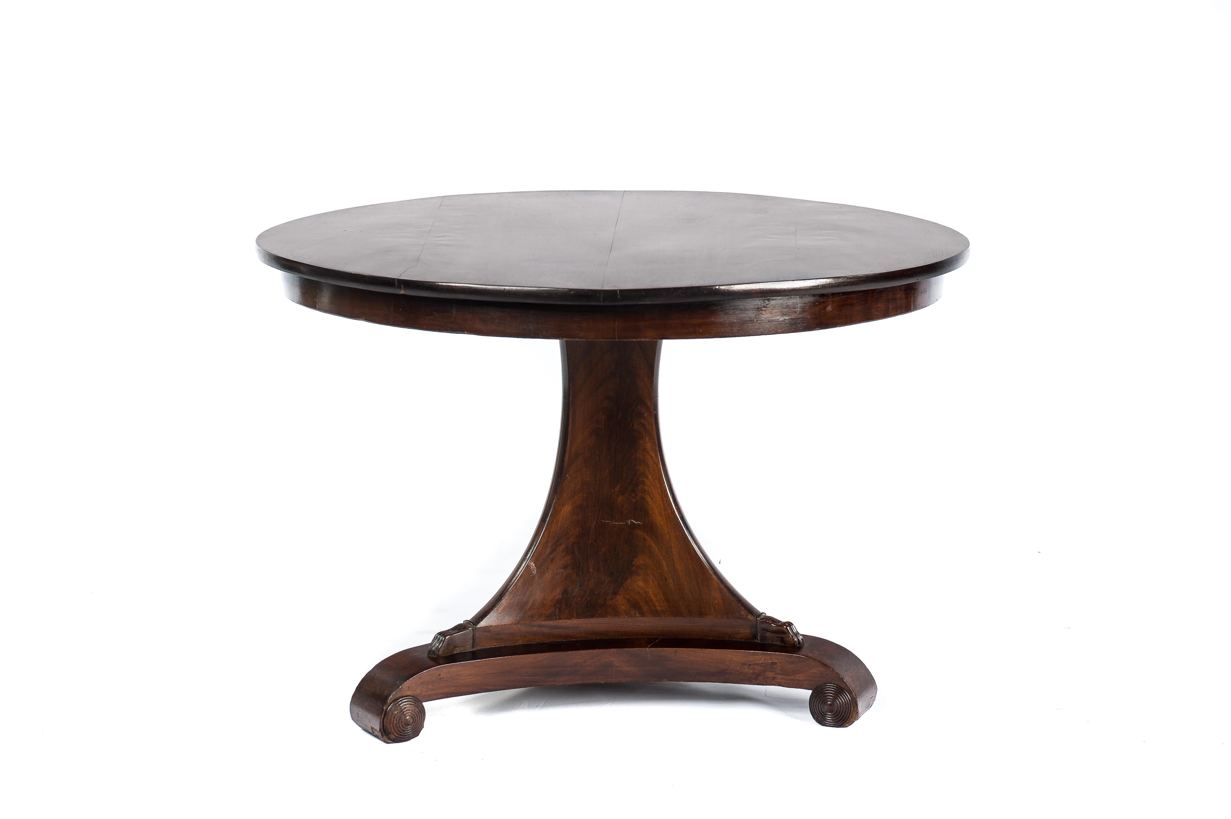 A beautiful round mahogany dining table on a trefoil platform base that ends in elegant scrolls. The base has an elegant triangular column that ends in claw feet to support the tabletop. The tabletop is made in 0.8-inch thick solid mahogany in a