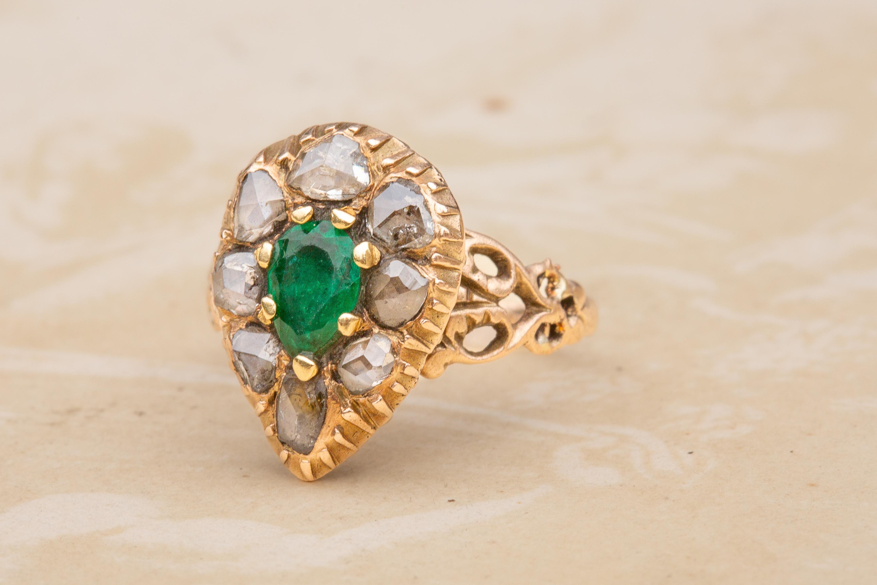 A gorgeous antique emerald and diamond ring dating to the 19th century. The central prong-set 0.3ct pear cut natural emerald displays a gorgeous lush green hue and great saturation. It is surrounded by a halo of rose cut diamonds in closed-back and