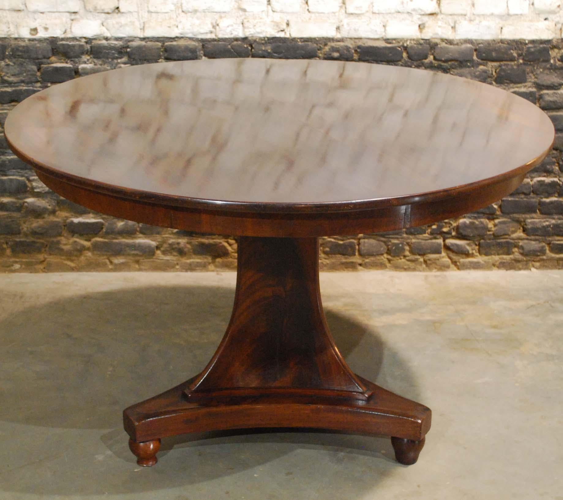 An elegant round mahogany dining table on a trefoil platform base that stands on bun feet. 
The tabletop is made in 0.8-inch thick solid mahogany in a “livre ouvert” style. It is made in two pieces of timber that fold open like a book and are