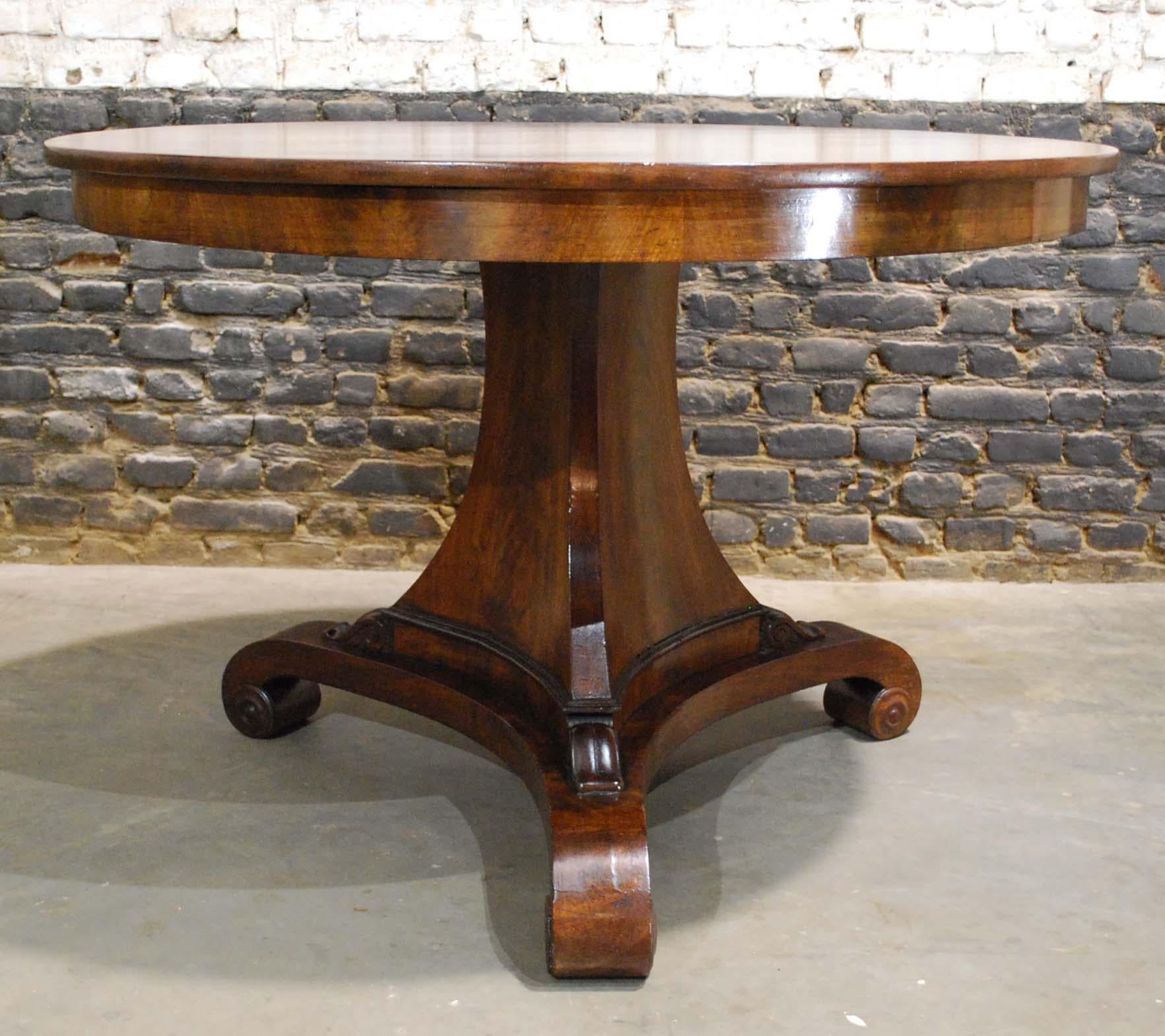 A beautiful round mahogany dining table on a trefoil platform base that ends in elegant scrolls.
The base has an elegant triangular column that ends in carved feet to support the tabletop. The tabletop is made in 0.7-inch thick solid mahogany in a