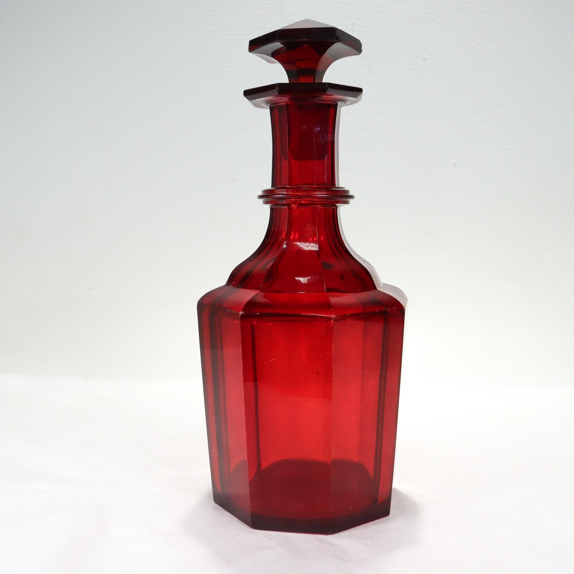 A fine antique wine decanter.

Likely English in origin.

In ruby red cut glass with 8 faceted sides, with an applied ring to its neck, and with a conforming stopper. 

The base has a polished pontil mark and an old sticker. 

Matching painted 'X's