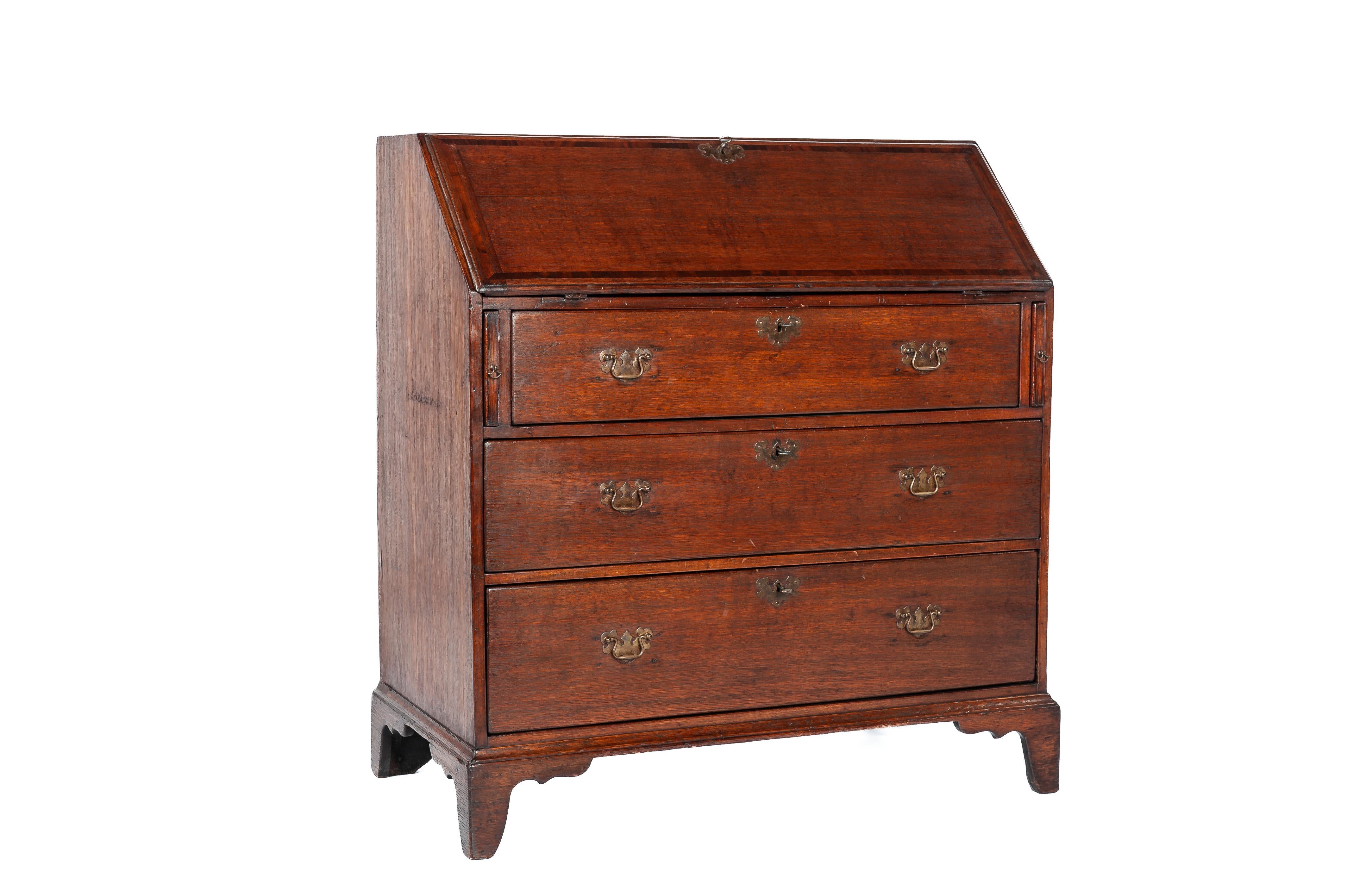 Presented here is a stunning antique slant-front secretary desk crafted in oak wood in England in the late 19th century, circa 1870. The desk features three drawers with a pine interior, adorned with beautifully shaped brass fittings and equipped