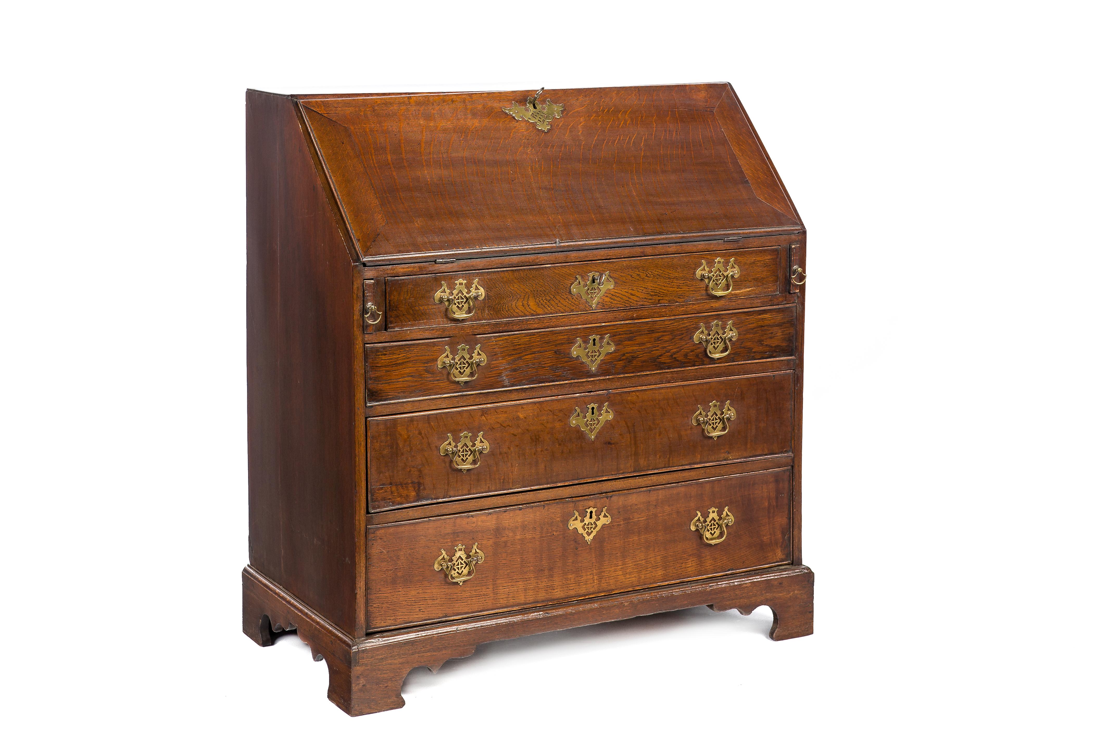 This classic slant front desk or bureau was made in England in the early 19th century. 
It was made in the finest quality watered European oak. The secretary is elevated on bracket feet. It features four drawers fitted with the original brass ajour