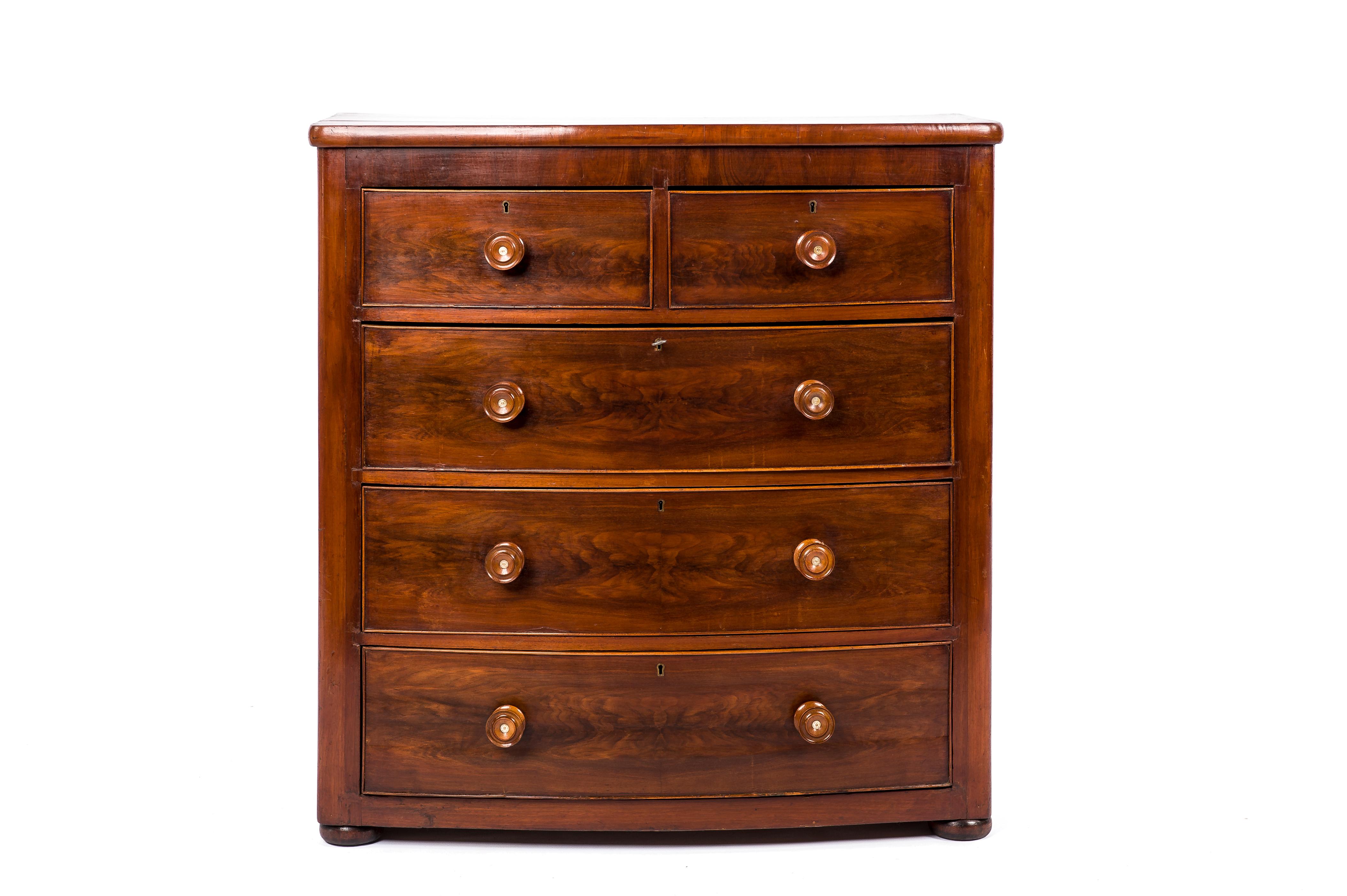 This beautiful sleek commode or chest of drawers was made in England in the late 19th century, circa 1840. The piece has a bow front that houses five drawers in total all of which are equipped with a working lock. A key that fits all locks is