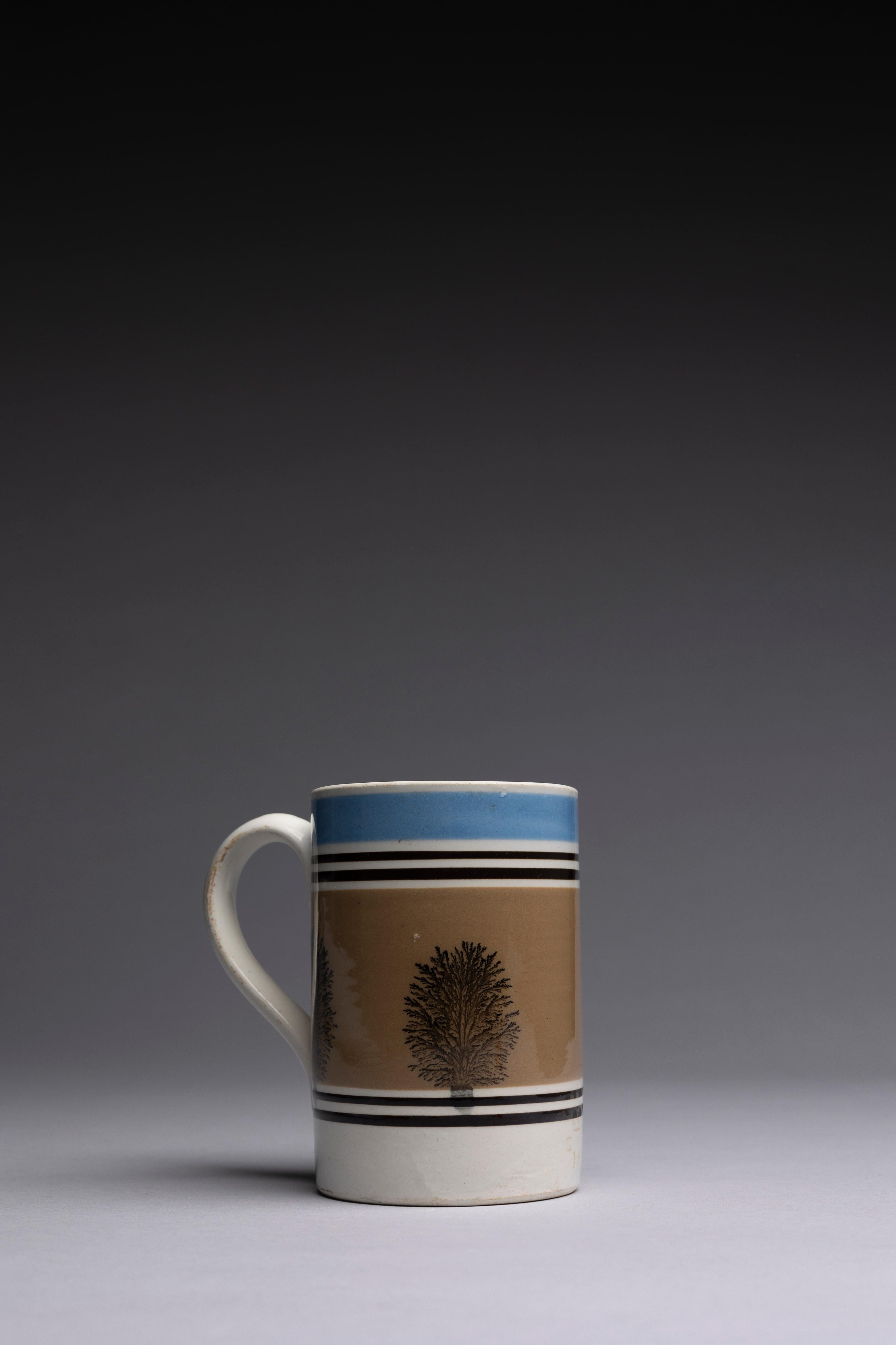 Ein englischer Mochaware-Becher mit schwarzen und blauen maschinell gedrehten Bändern und einem Baummuster auf einer weichen braunen Glasur.

Dieser große Becher aus Mokkaware zeigt schwarze und blaue Rauten, die ein baumartiges Muster (Algen
