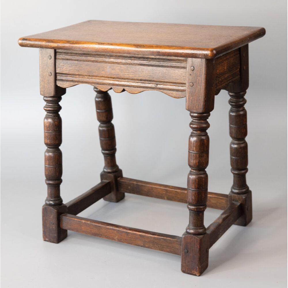A superb antique 19th-Century English oak pegged joint stool with beautiful patina and hand turned legs, stretchers, and lovely hand carved scalloped apron. This charming stool would be great for extra seating and also perfect as a side table for