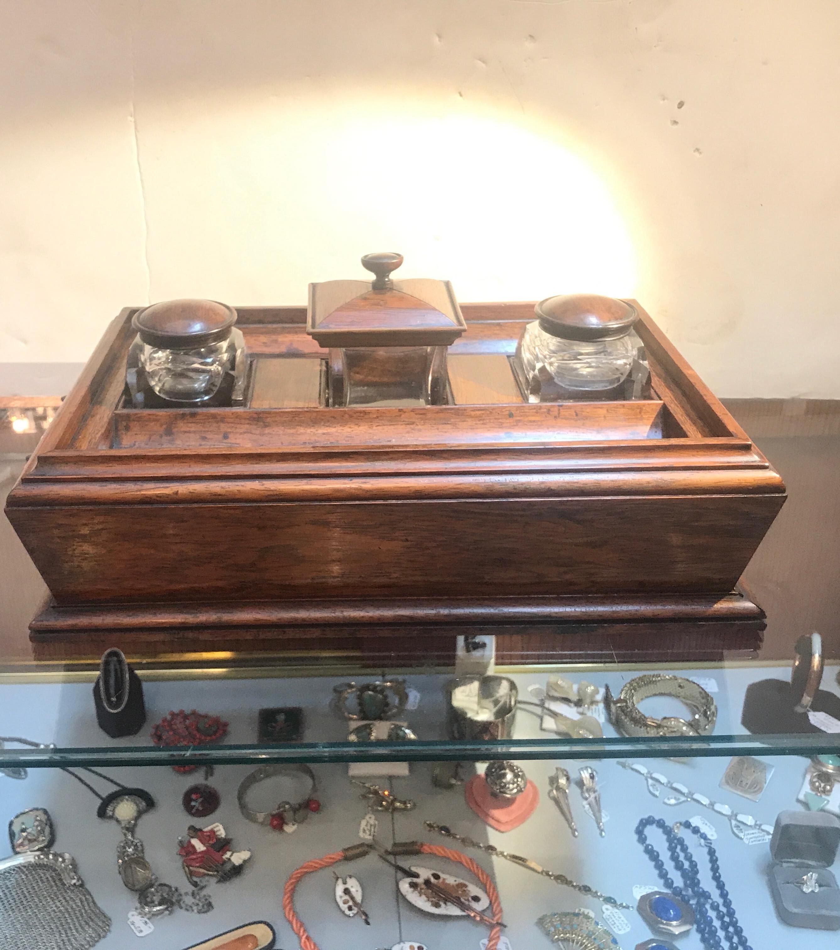Beautiful rosewood inkstand with 2 glass inkwells with a center square glass canister. The top with a place for pens on the front and back with a slim drawer for paper. Each side with cast patinated bronze handles. The inkwells and canister with