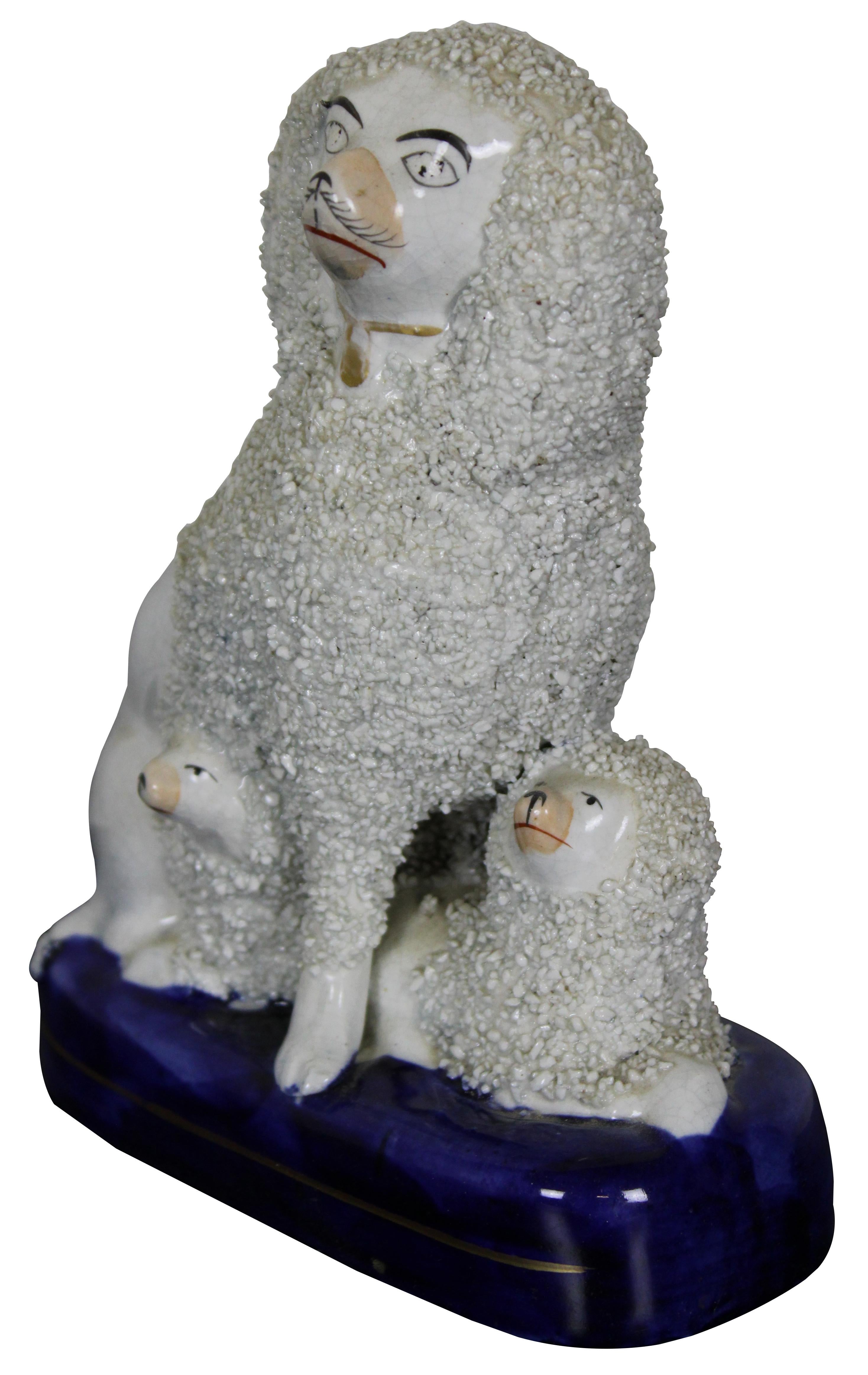 Antique mid 19th century Staffordshire porcelain trio figurine of a white Spaniel or Poodle and two puppies, seated on a cobalt blue base with textured confetti design. Measure: 7