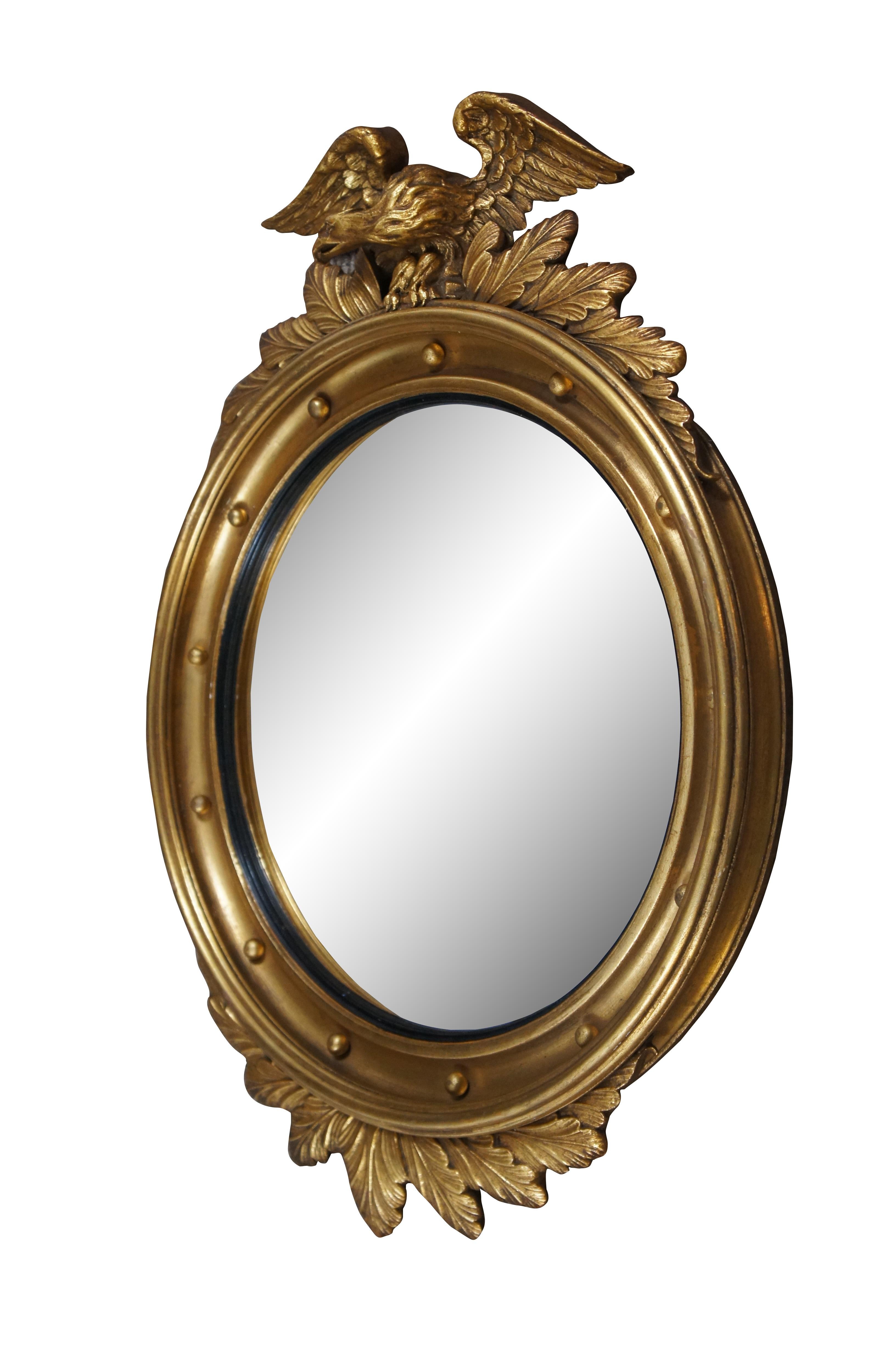 Antique 19th Century gold giltwood bullseye / convex wall mirror featuring a round frame carved with an American eagle with wings outstretched and bunches of acanthus leaves, over a beveled and braded frame with a black inner border around the