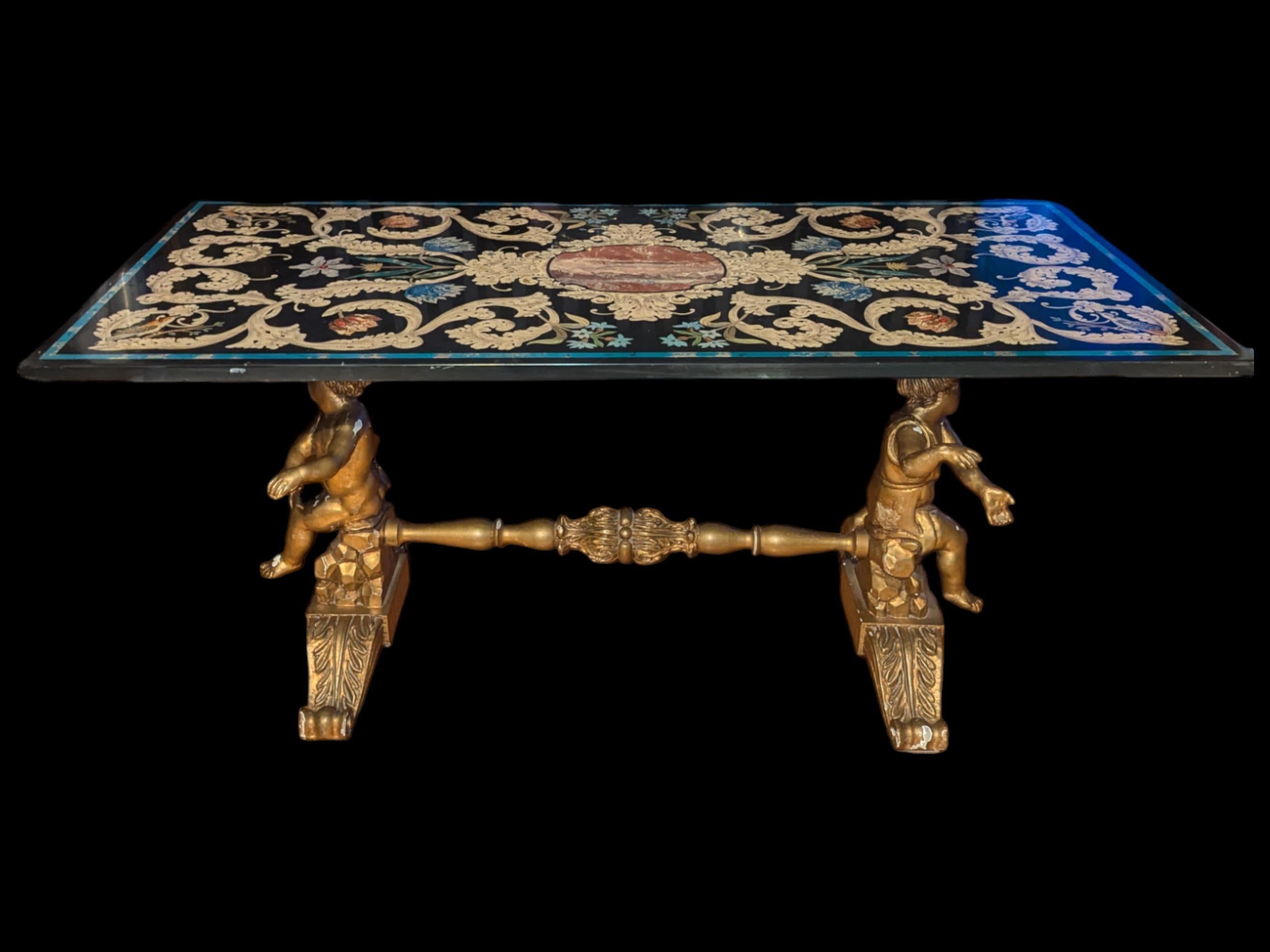 Esta exquisita mesa antigua presenta un diseño ornamentado que capta la esencia de la artesanía opulenta. El tablero, probablemente fabricado en pizarra pintada para imitar la intrincada belleza de la *pietra dura*, muestra un elegante conjunto de