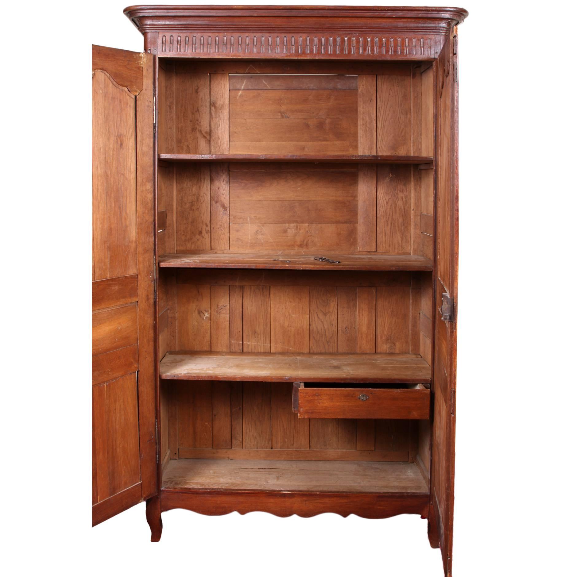 Antique French armoire, 19th century, double door with triple recessed and craved panels, the top ones shaped and carved, large carved overhanging cornice above a reeded frame, reeded side supports and carved side panels, opens to reveal storage