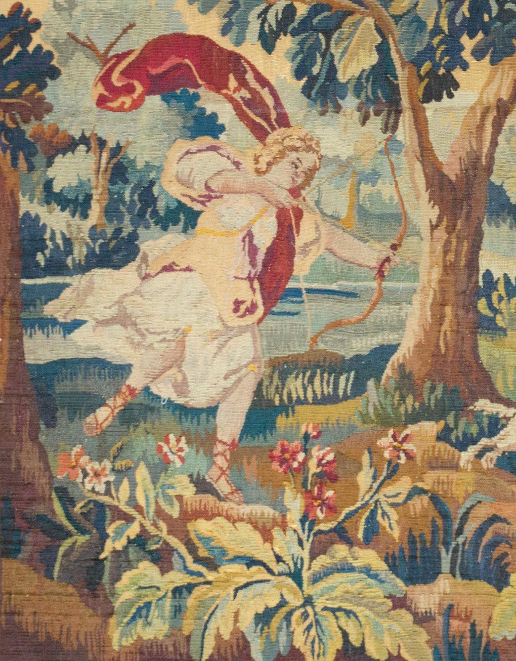 Tapisserie de verdure française ancienne du 19ème siècle représentant un paysage immaculé et charmant sur les rives d'une rivière avec Cupidon chassant le cerf. La scène est entourée de terrains verdoyants et fleuris, d'un château et de montagnes au