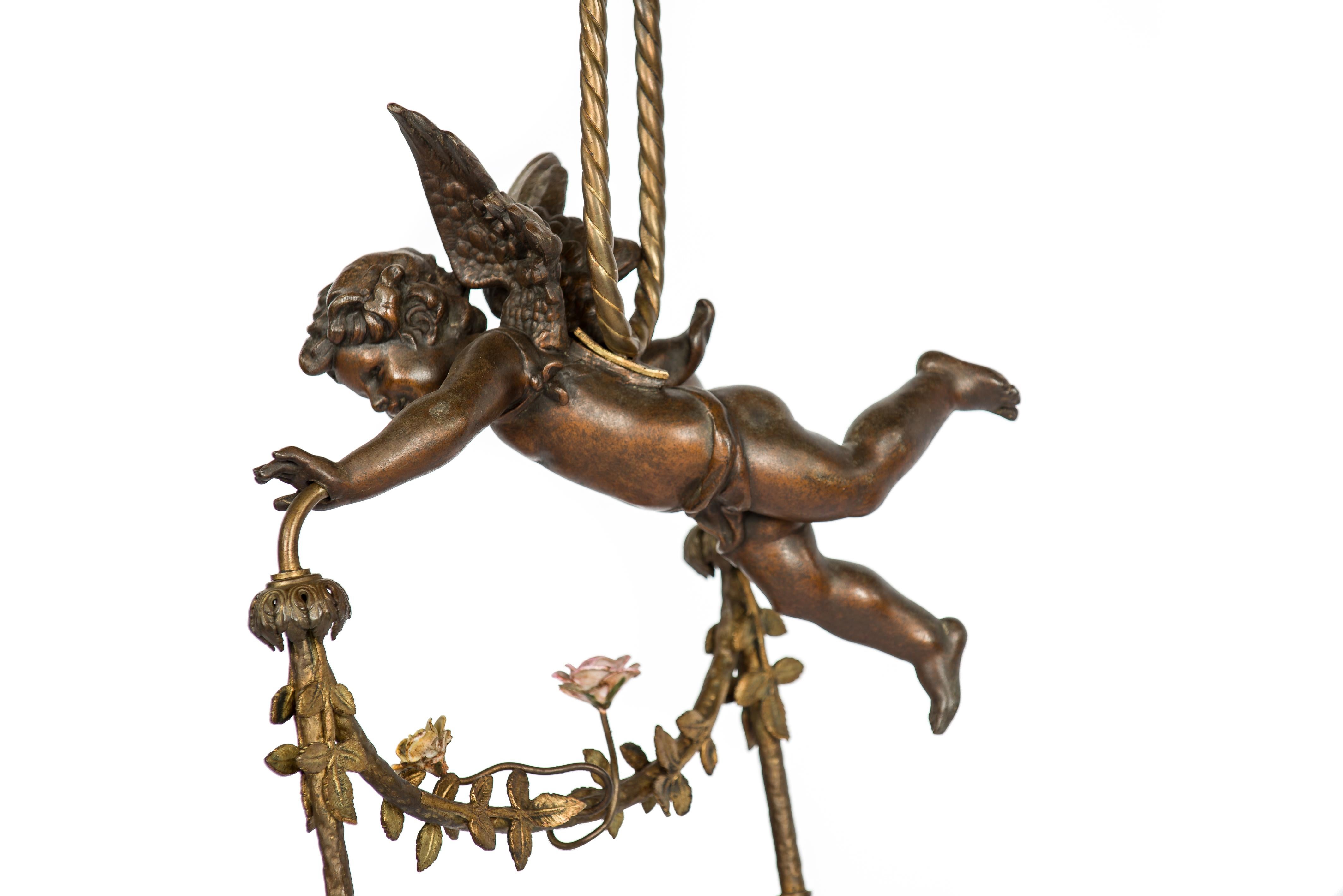 A classic cast brass angel or putti pendant light made in France in the late 19th century circa 1890.
The angel, also known as a cherub holds a delicate floral garland adorned with two delicate porcelain flowers and ends in two etched glass shades