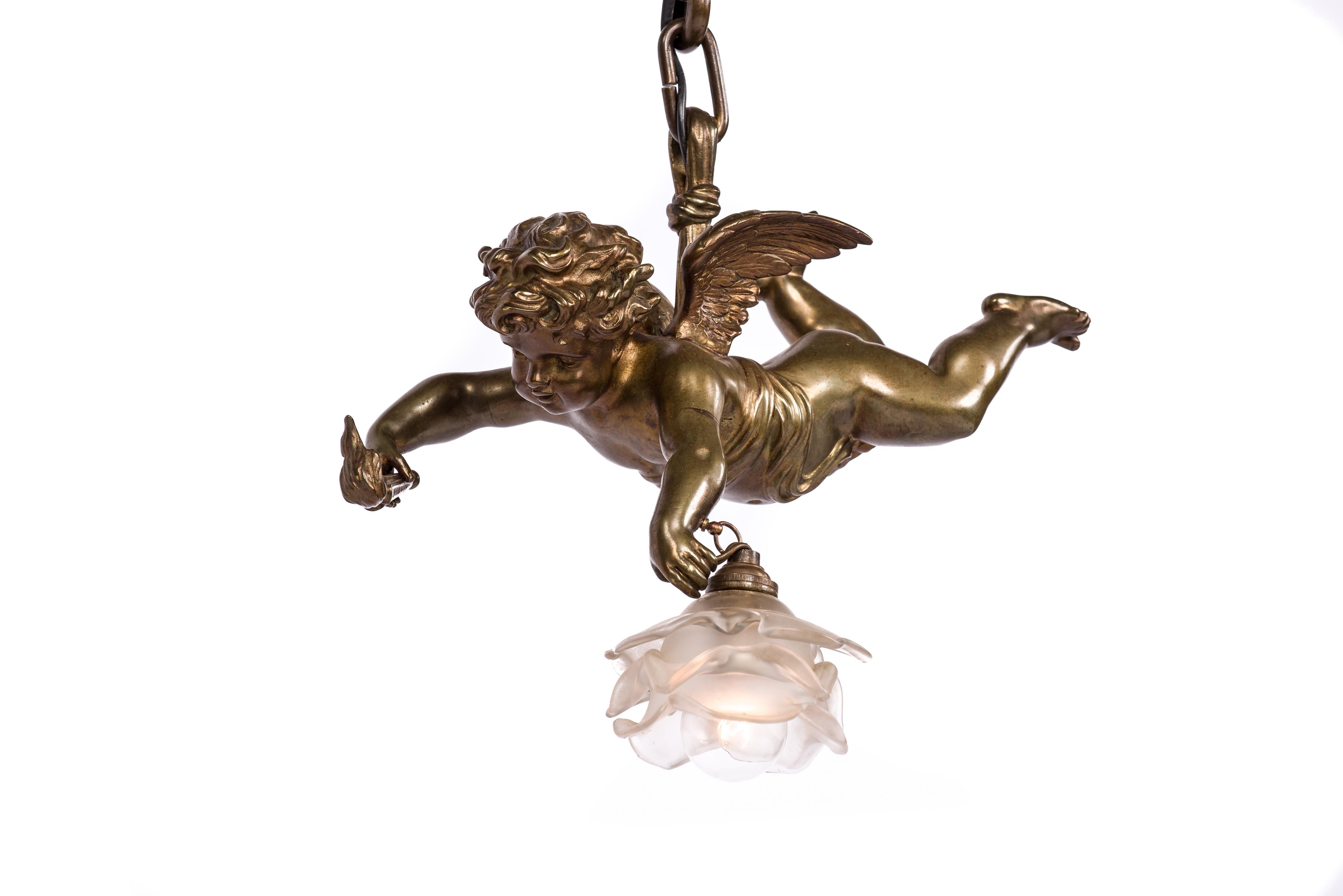A classic cast brass angel or putti pendant light made in France in the late 19th century. 
The angel, also known as a cherub holds a flaming torch in one hand and an etched glass shade in the shape of a rose in the other. The flame of the Olympic
